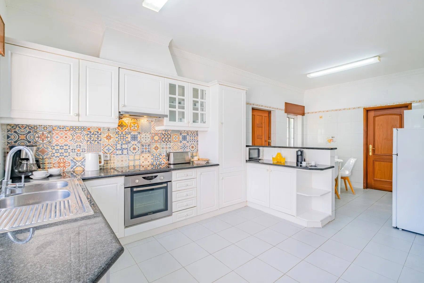Una cocina luminosa con gabinetes blancos, salpicadero de azulejos y una barra central.