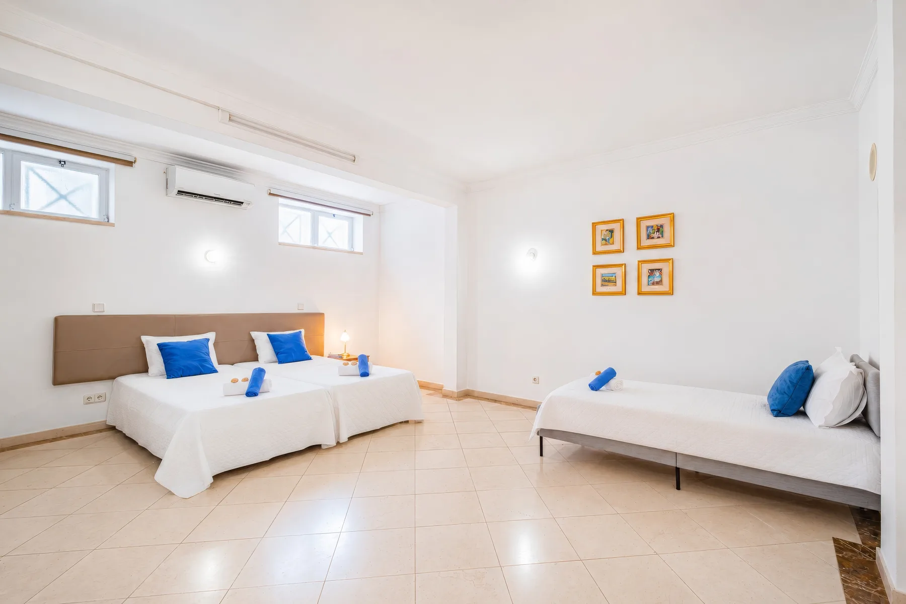 Un dormitorio luminoso con dos camas, ropa de cama blanca y cojines azules.