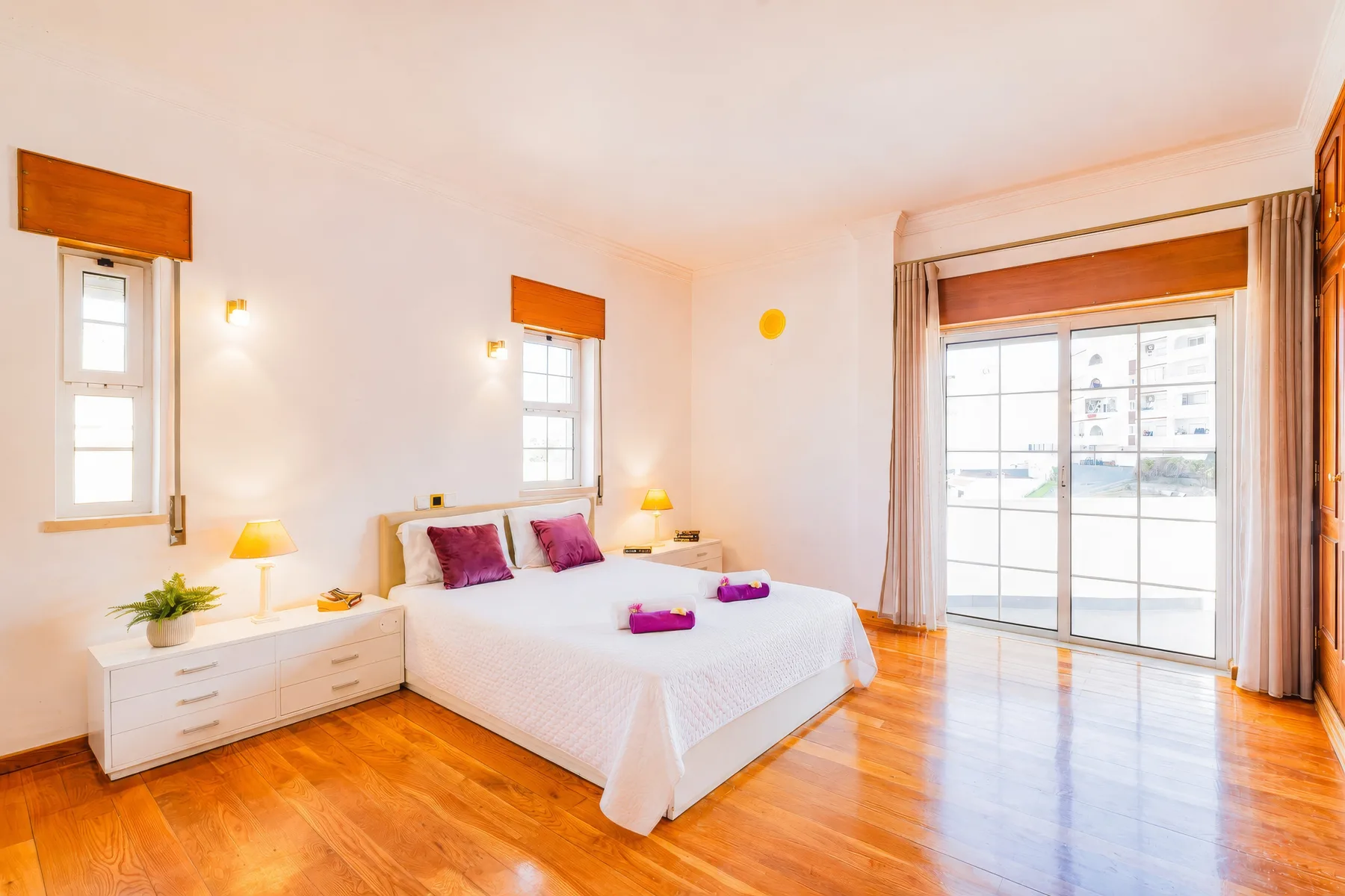 Un dormitorio luminoso con una cama, mesitas de noche y una gran puerta de cristal.