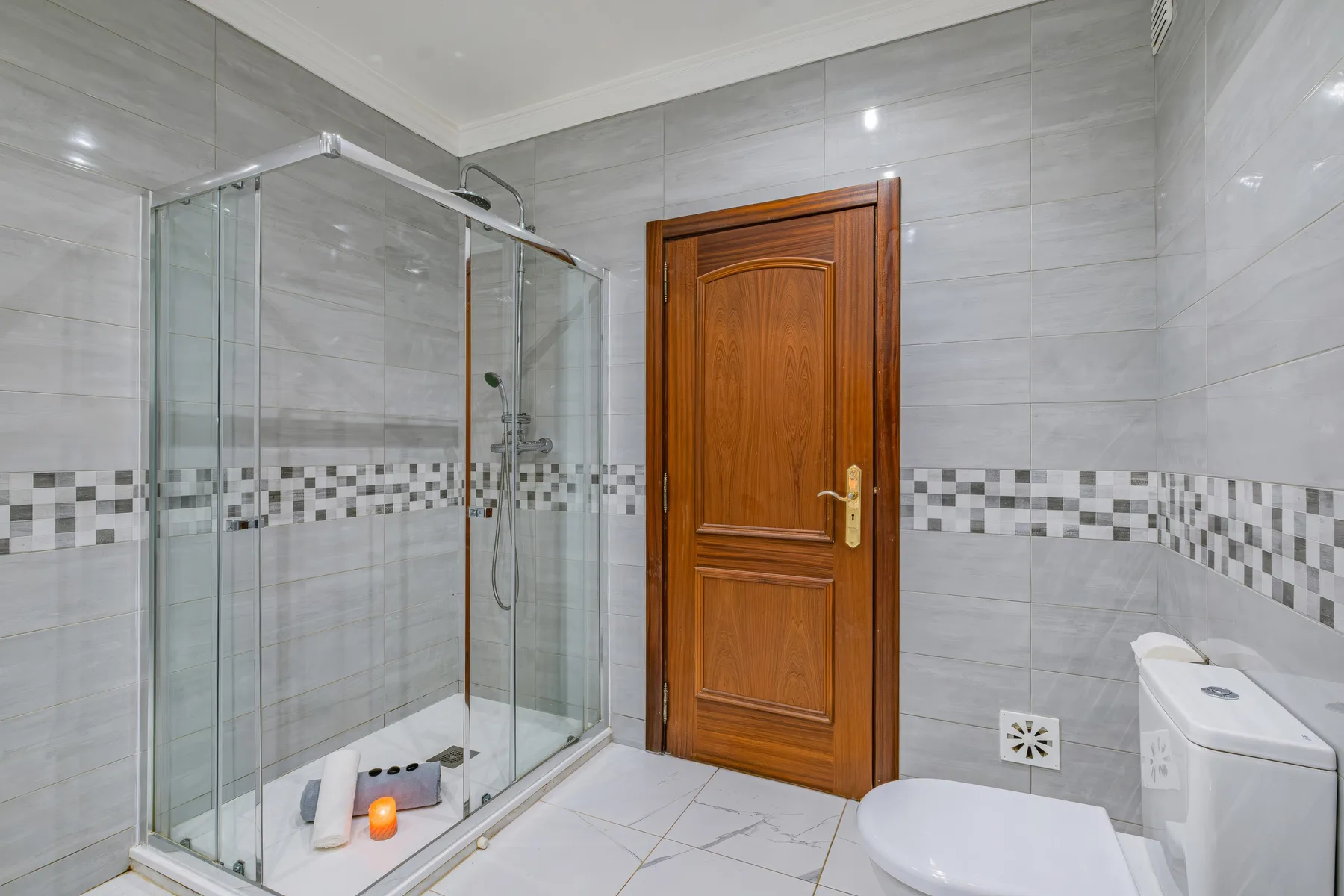 Un baño alicatado con ducha de vidrio, puerta de madera e inodoro.