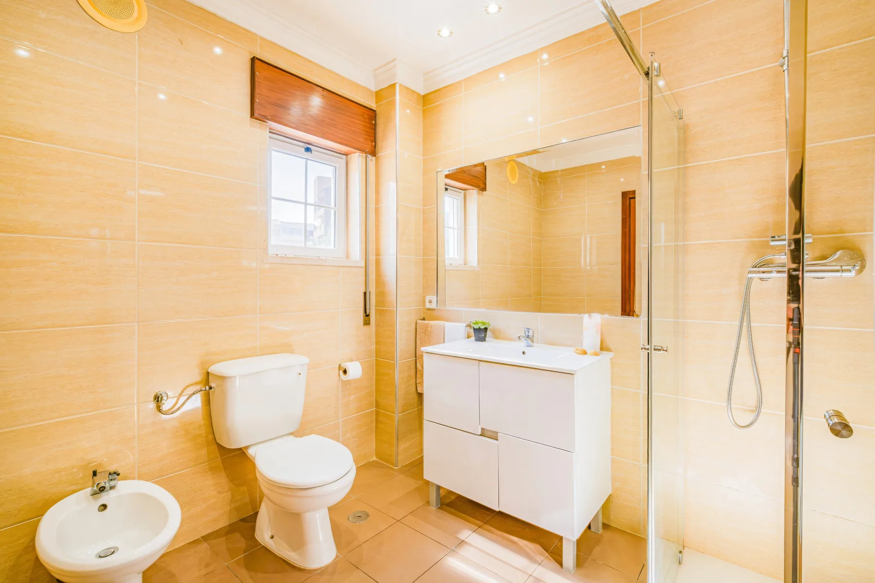Un baño luminoso con azulejos, lavabo con mueble, inodoro y ducha de vidrio.