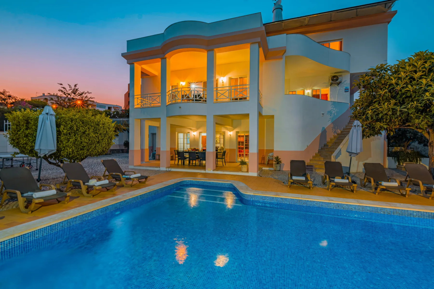 Una villa moderna da a una piscina, con asientos al aire libre alrededor del agua.