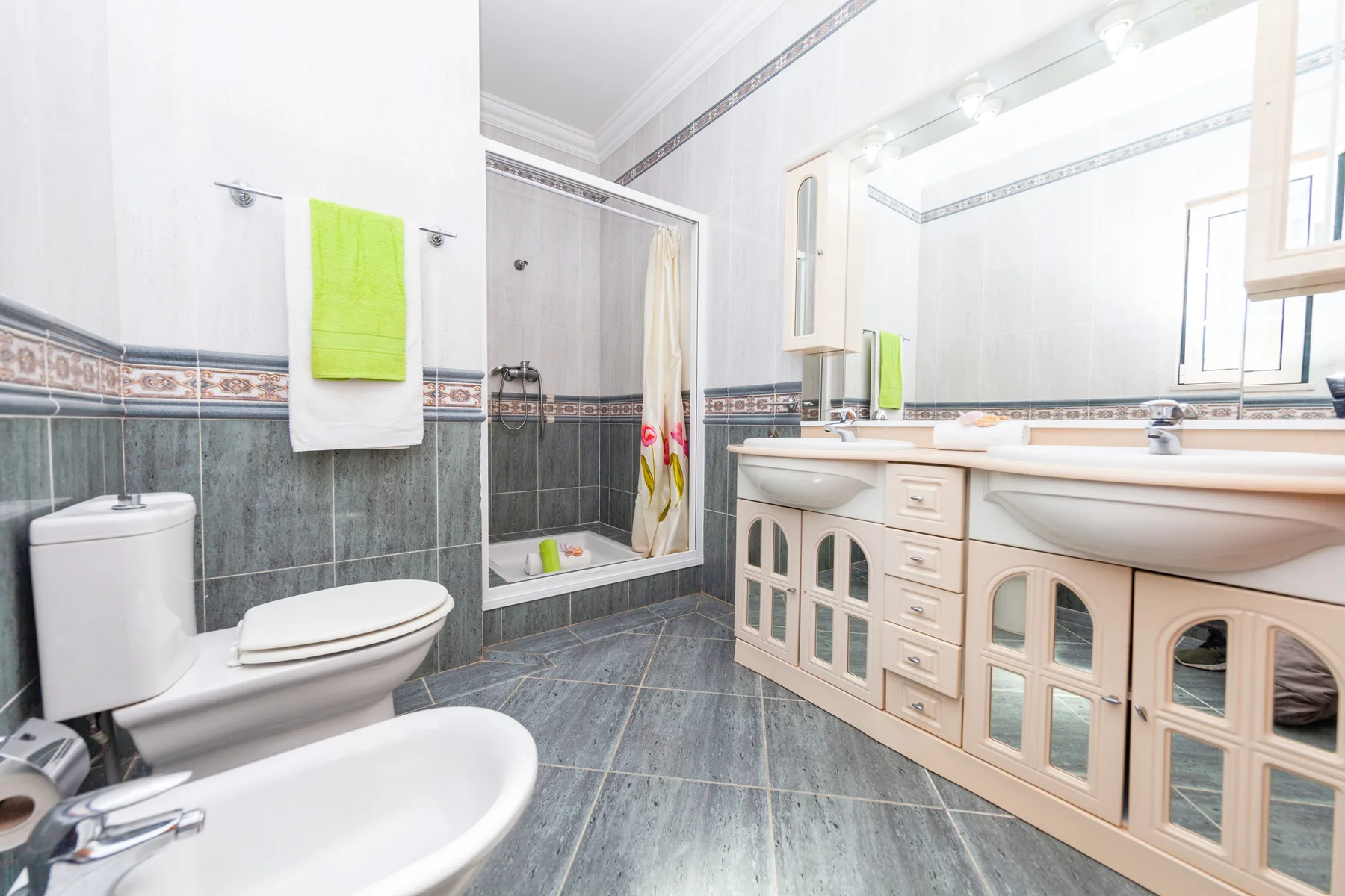 Un baño luminoso con azulejos, ducha, bañera y un largo tocador.