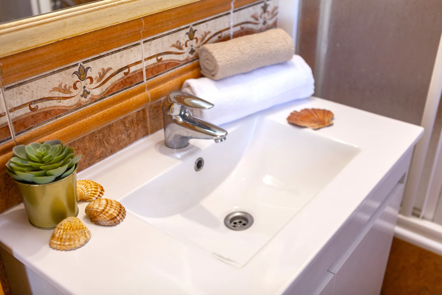Un lavabo de baño con toallas dobladas y azulejos decorativos en la pared.