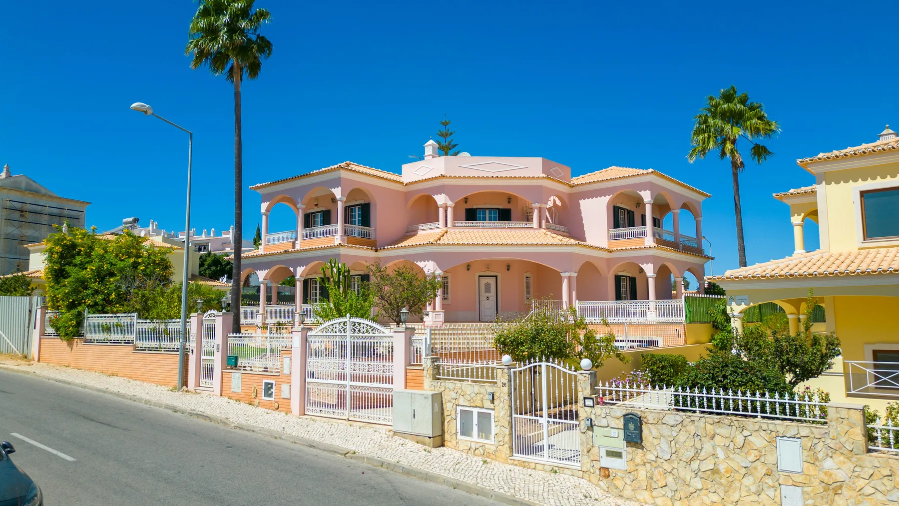 Una casa rosa de dos plantas con balcones arqueados se alza tras un muro de piedra con rejas.