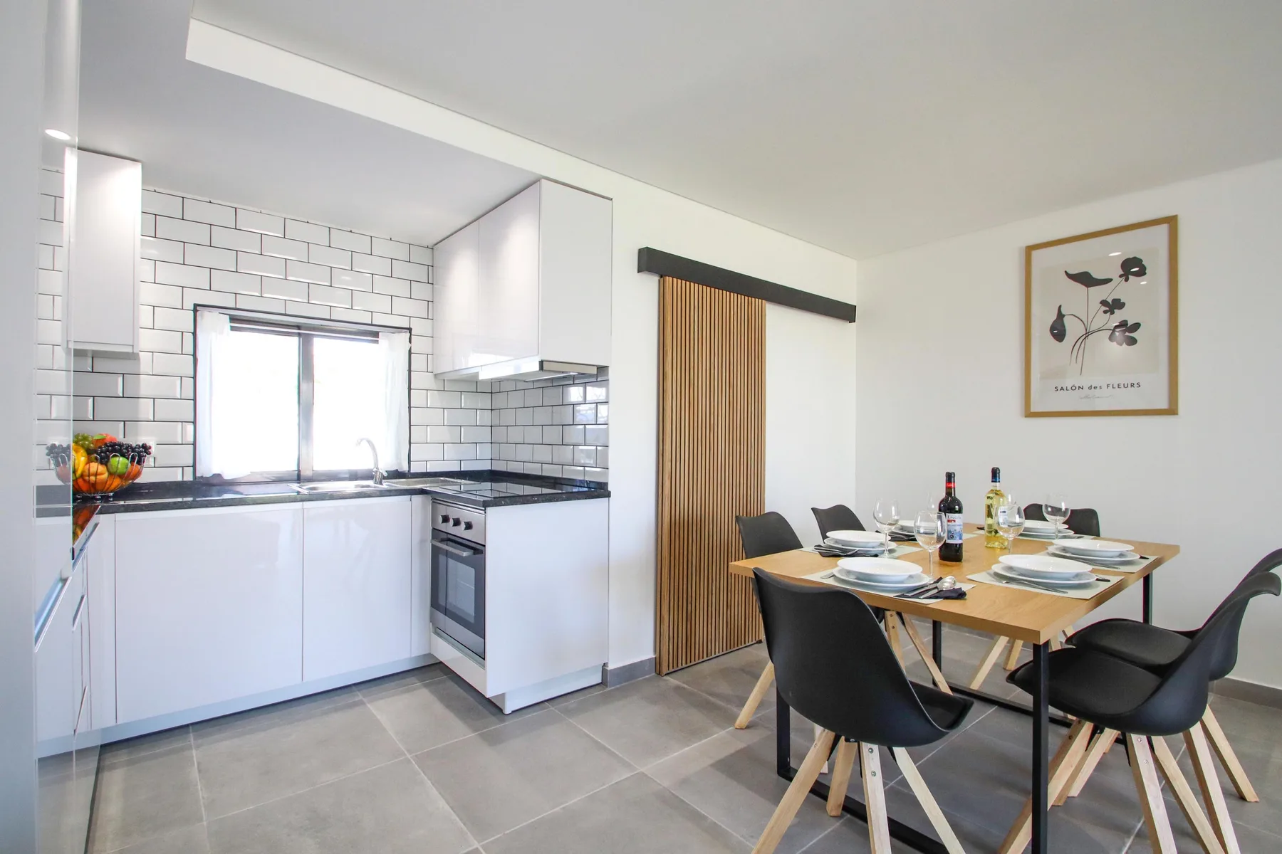 Una luminosa cocina y comedor con armarios blancos y una mesa de madera.