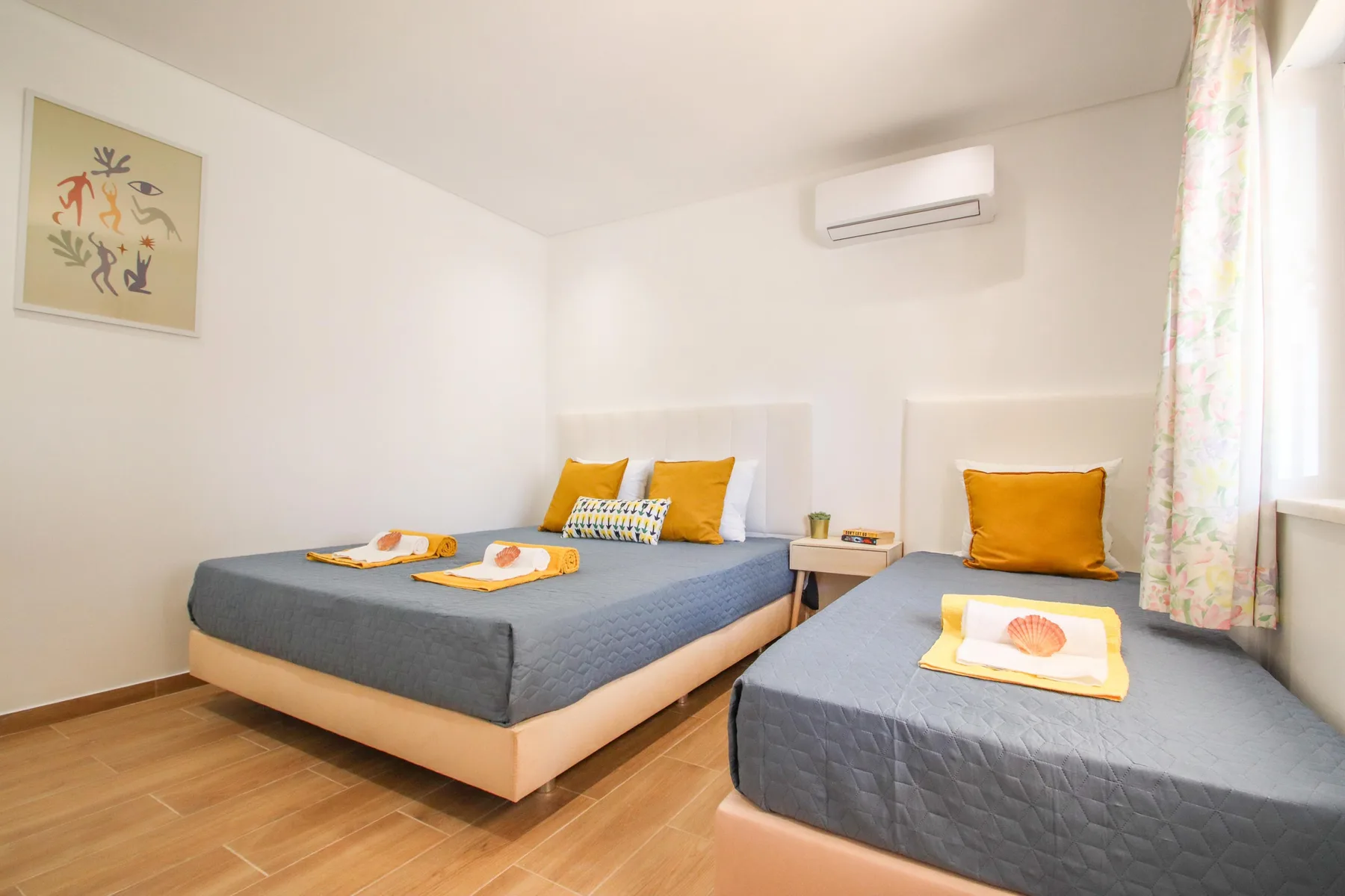 Un dormitorio con dos camas, cojines naranjas y una cortina floral.