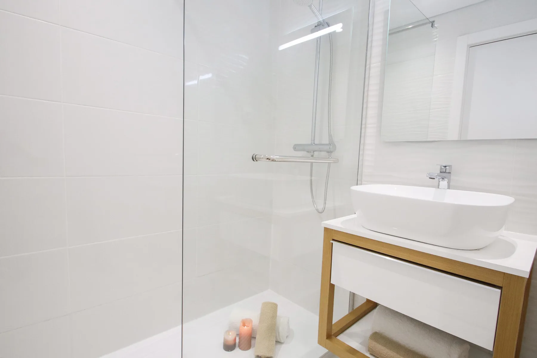 Un baño luminoso con una ducha de cristal y un lavabo blanco.
