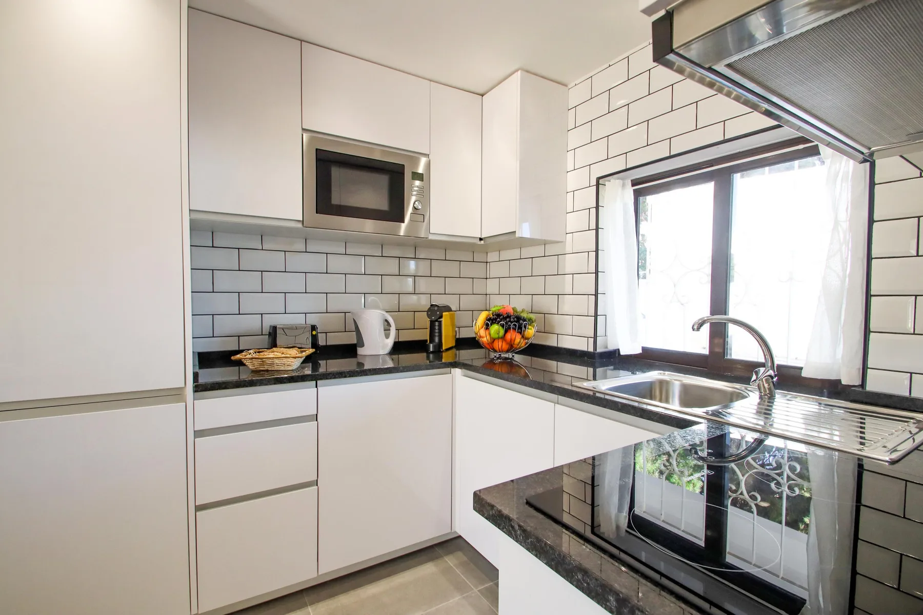 Una cocina moderna y luminosa con gabinetes blancos, paredes de azulejos y una superficie de cocción.