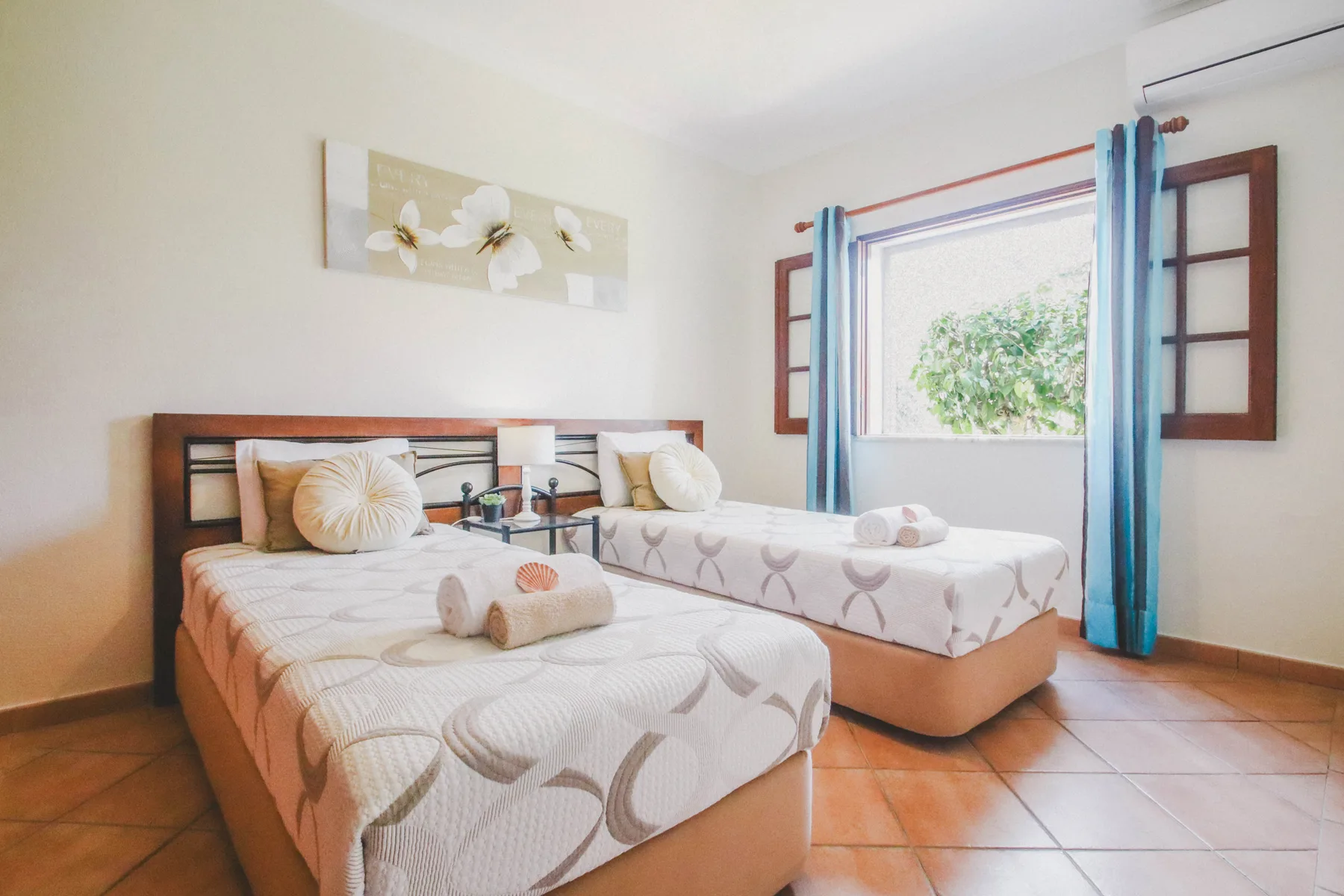Un dormitorio luminoso con dos camas, ropa de cama estampada y una ventana grande.