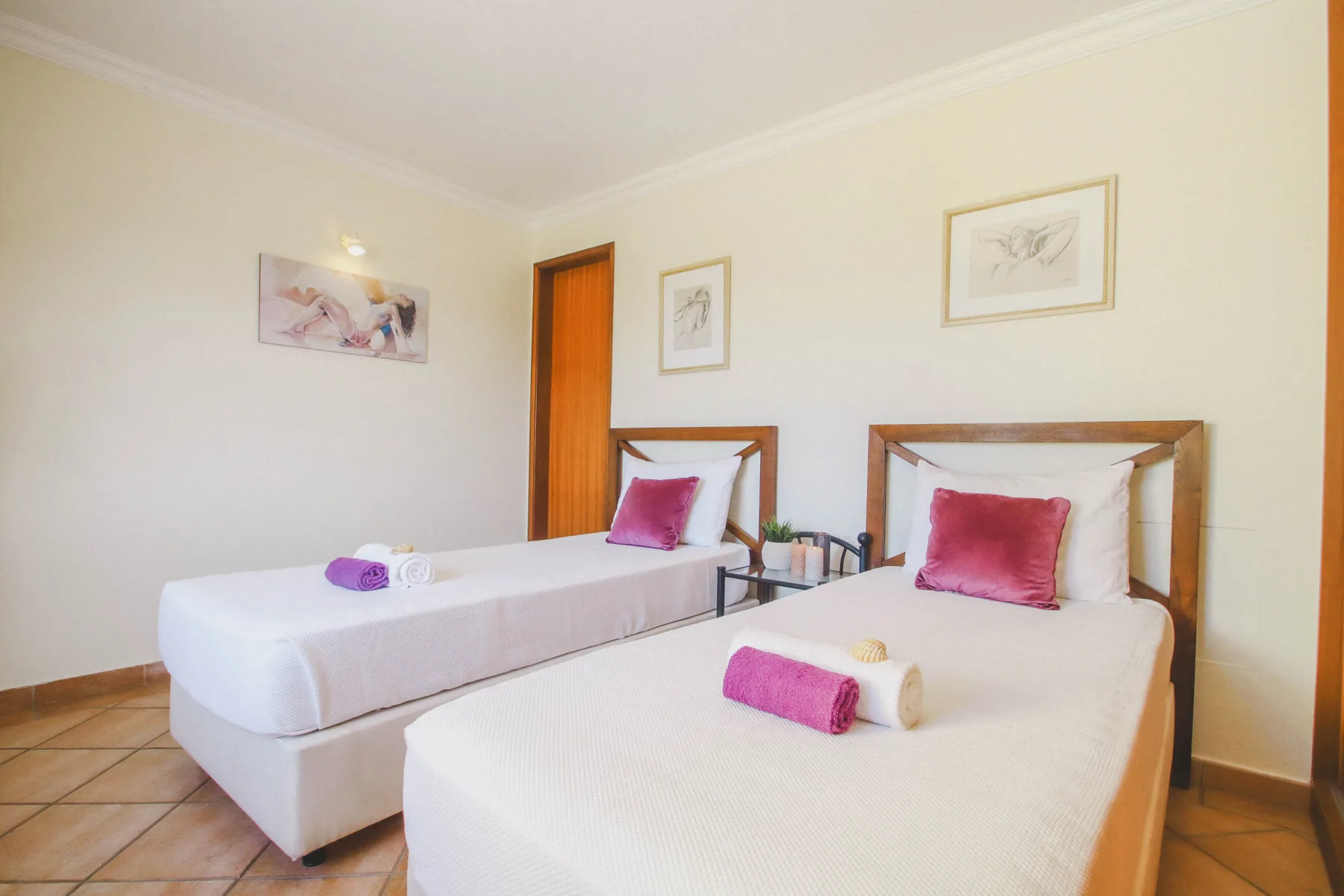 Un dormitorio luminoso con dos camas, ropa de cama blanca y cojines rosas.
