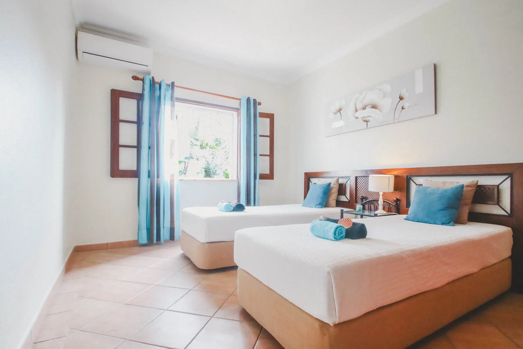 Un dormitorio luminoso con dos camas y cortinas azules junto a una ventana.