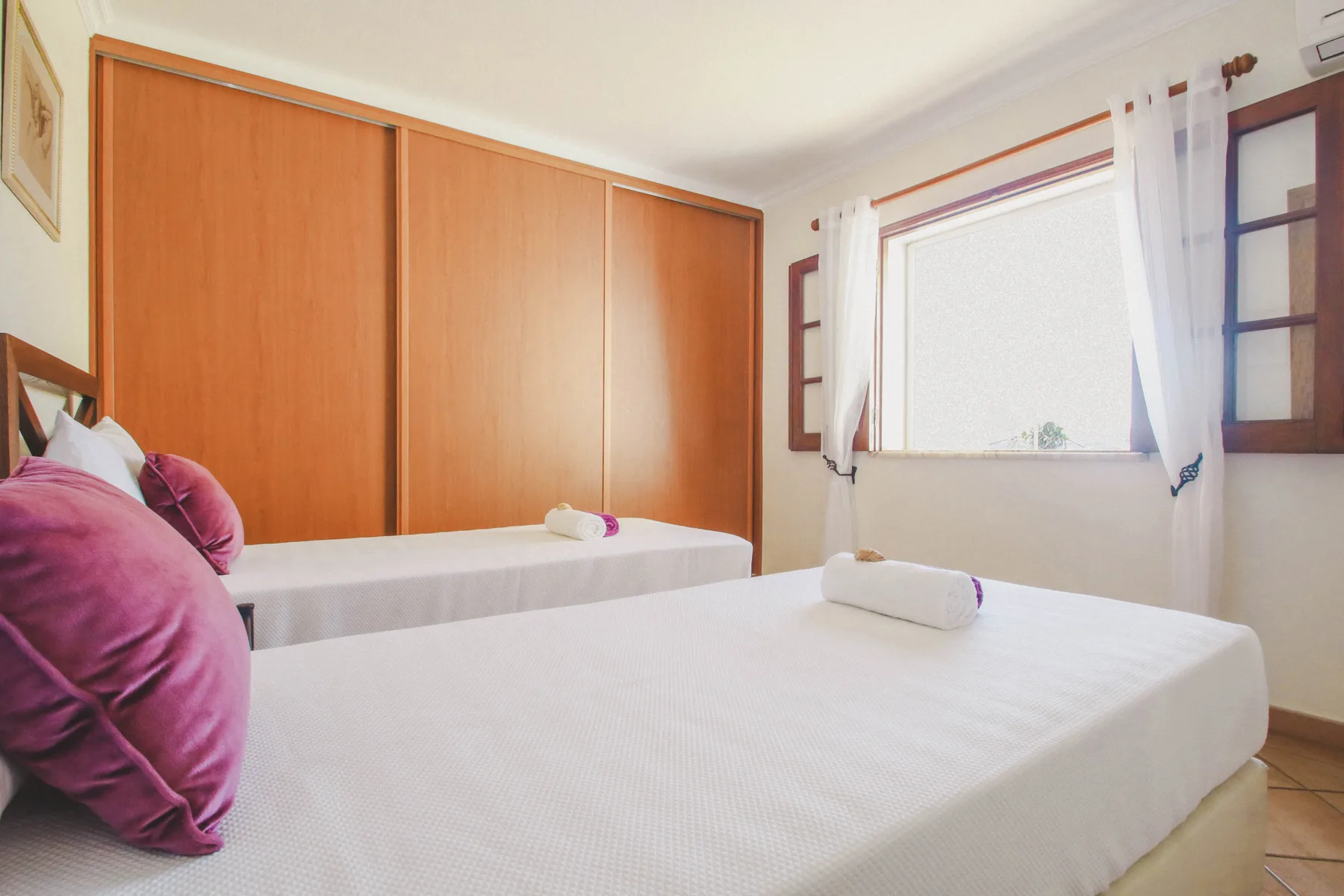Un dormitorio con dos camas y una ventana con cortinas blancas.