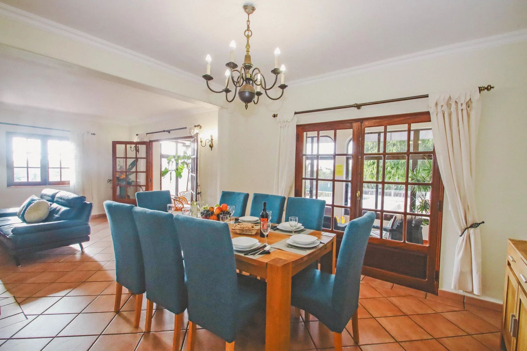 Un comedor con la mesa puesta y asientos tapizados azules junto a grandes ventanas.
