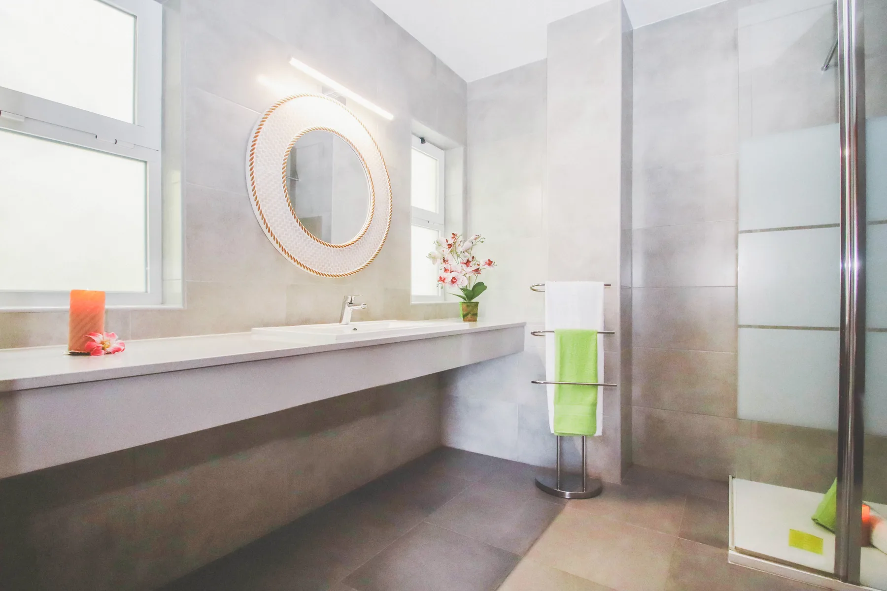 Un baño luminoso con una encimera larga, un espejo redondo y una ducha.
