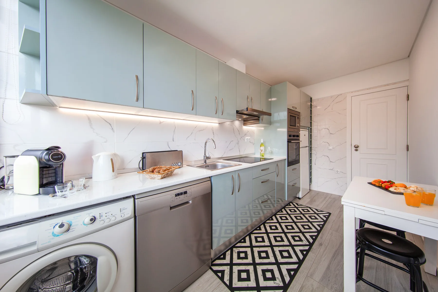 A bright kitchen with pale cabinets, a long countertop, and a patterned floor runner.