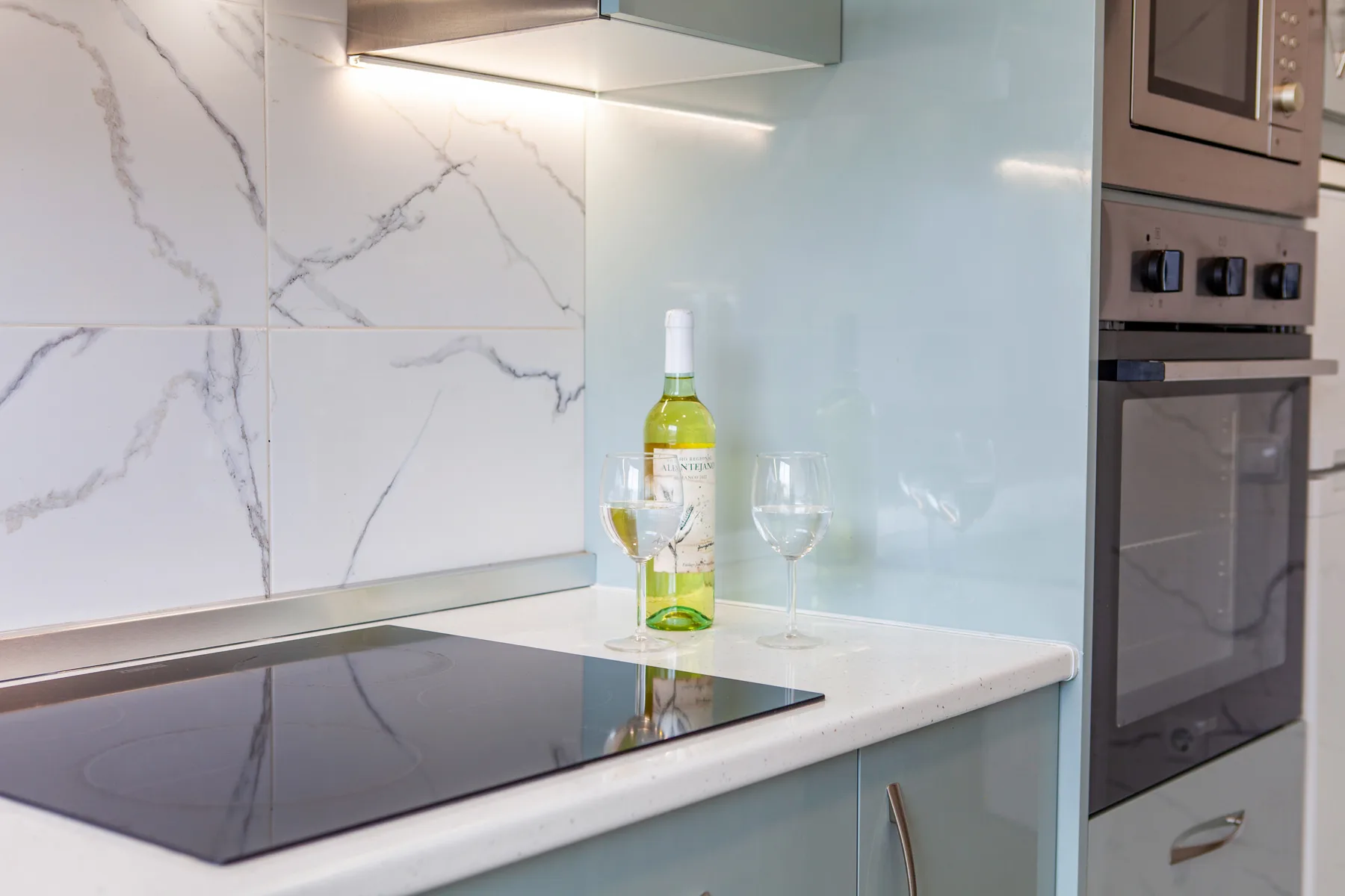 A modern kitchen counter with a cooktop, wine bottle, and glassware.