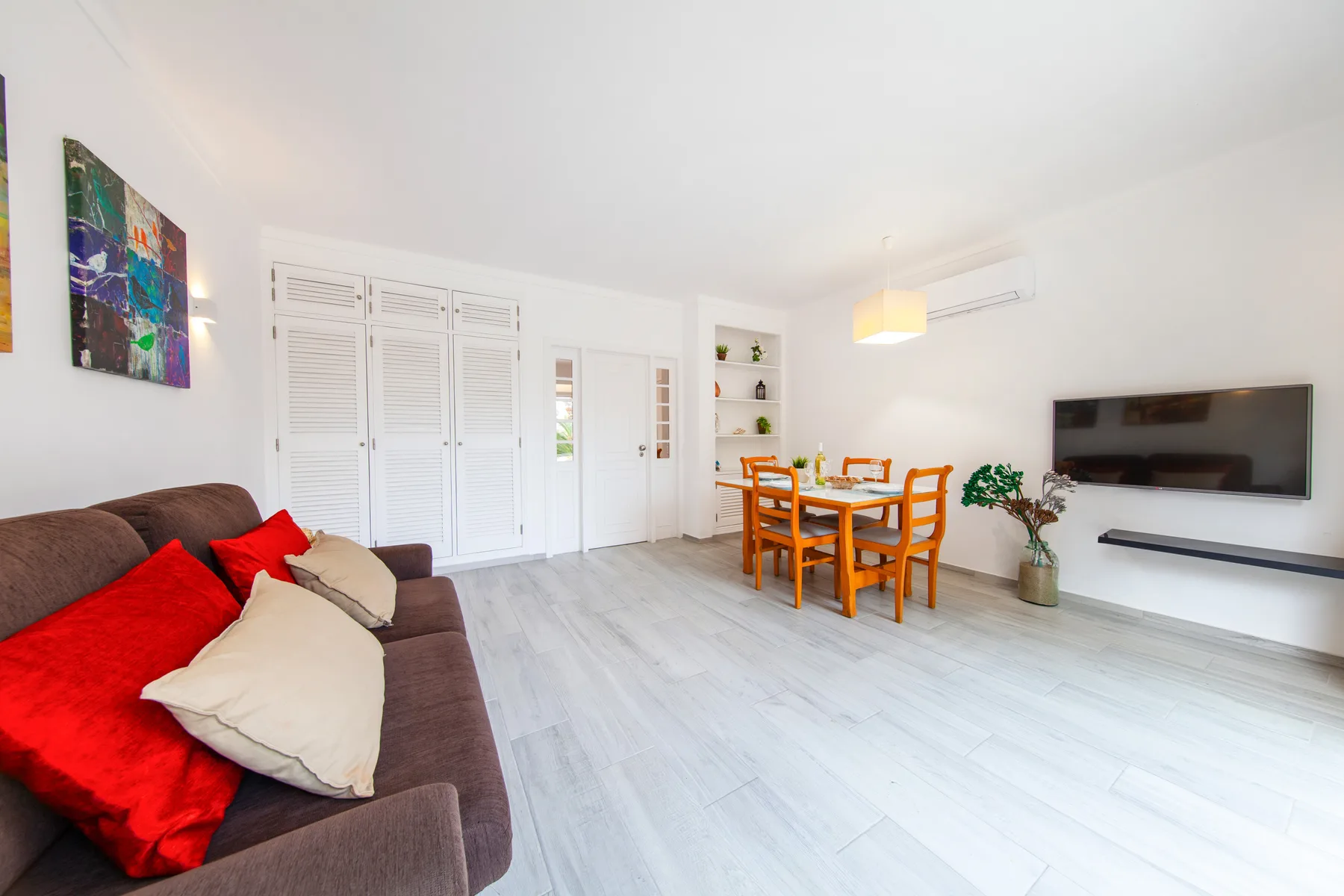 A bright living and dining area with seating, a dining table, and a wall-mounted television.