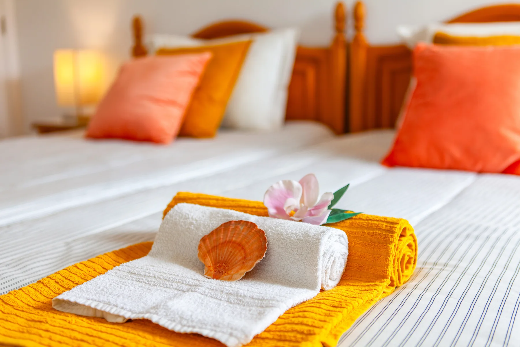 A bedroom with neatly made beds, colorful pillows, and folded towels.