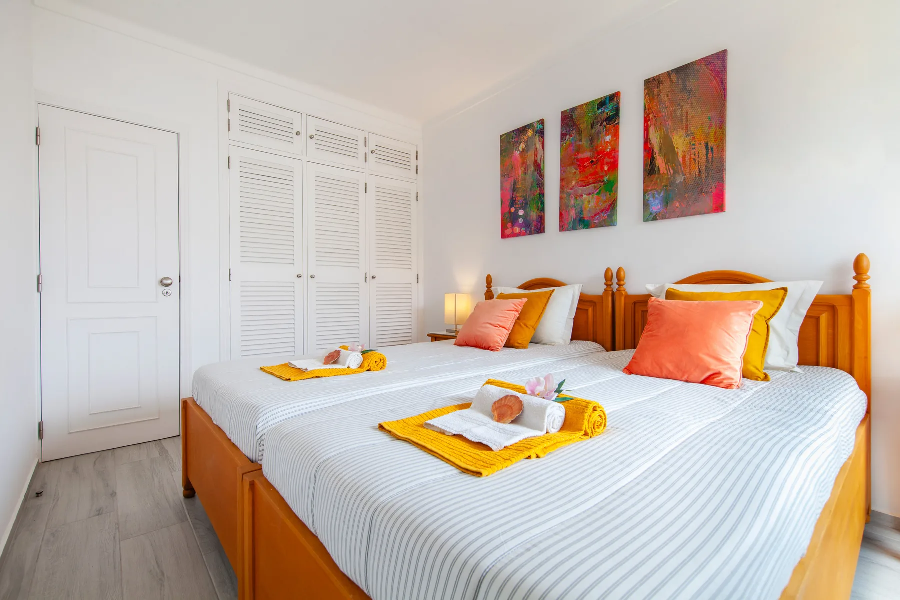 A bright bedroom with two beds, white bedding, and colorful abstract artwork.