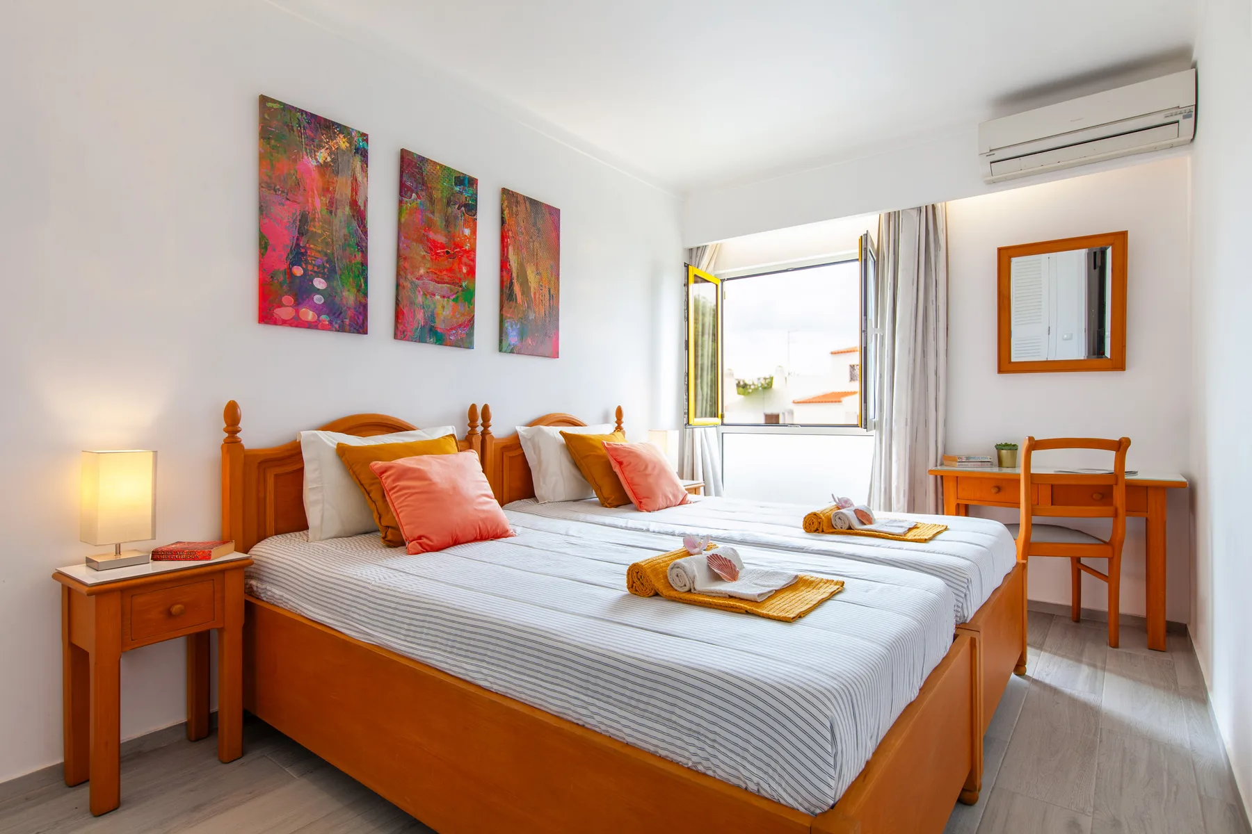 A bedroom with two beds, colorful wall art, and a window.