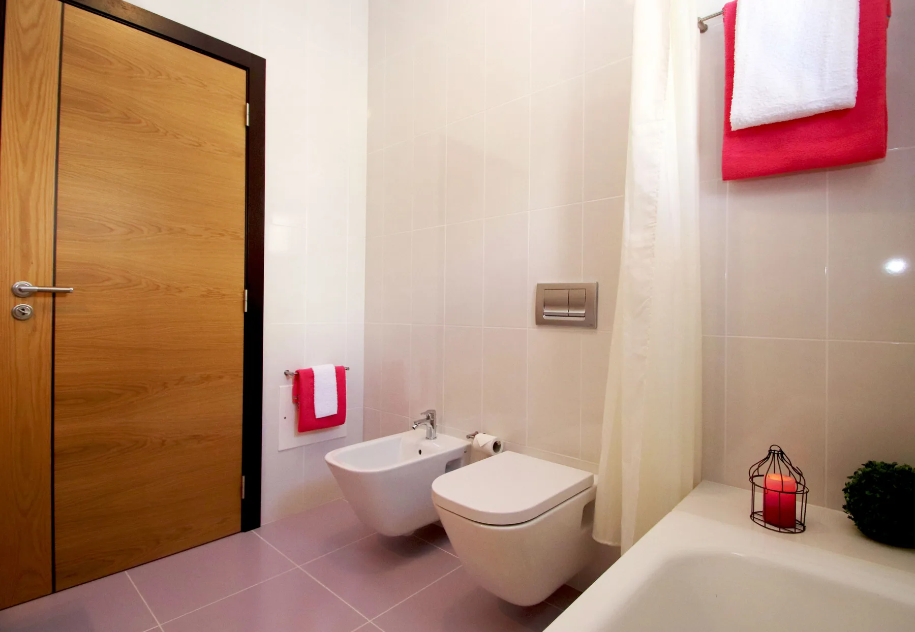 Un baño alicatado con puerta de madera, inodoro, bidé y bañera.