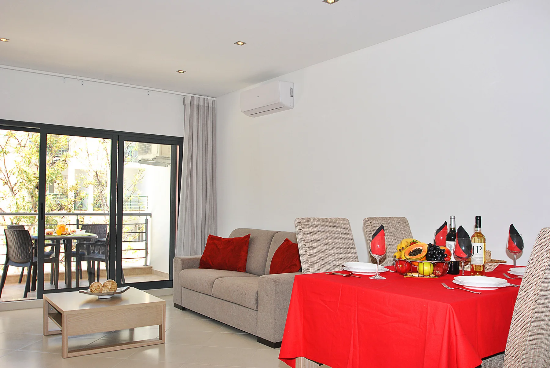 Una luminosa sala de estar y comedor con una mesa cubierta de rojo y asientos junto a puertas de cristal.