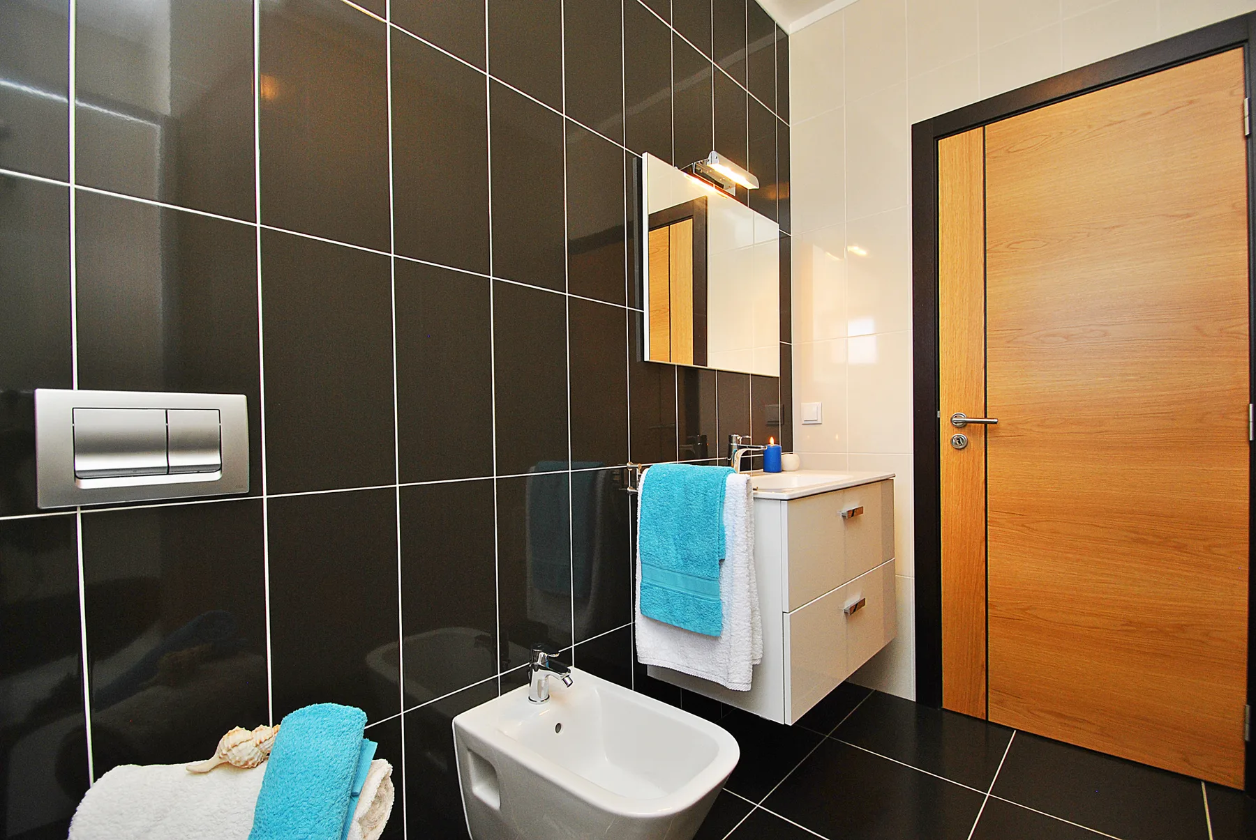 Un baño con lavabo de pared, espejo y puerta de madera.