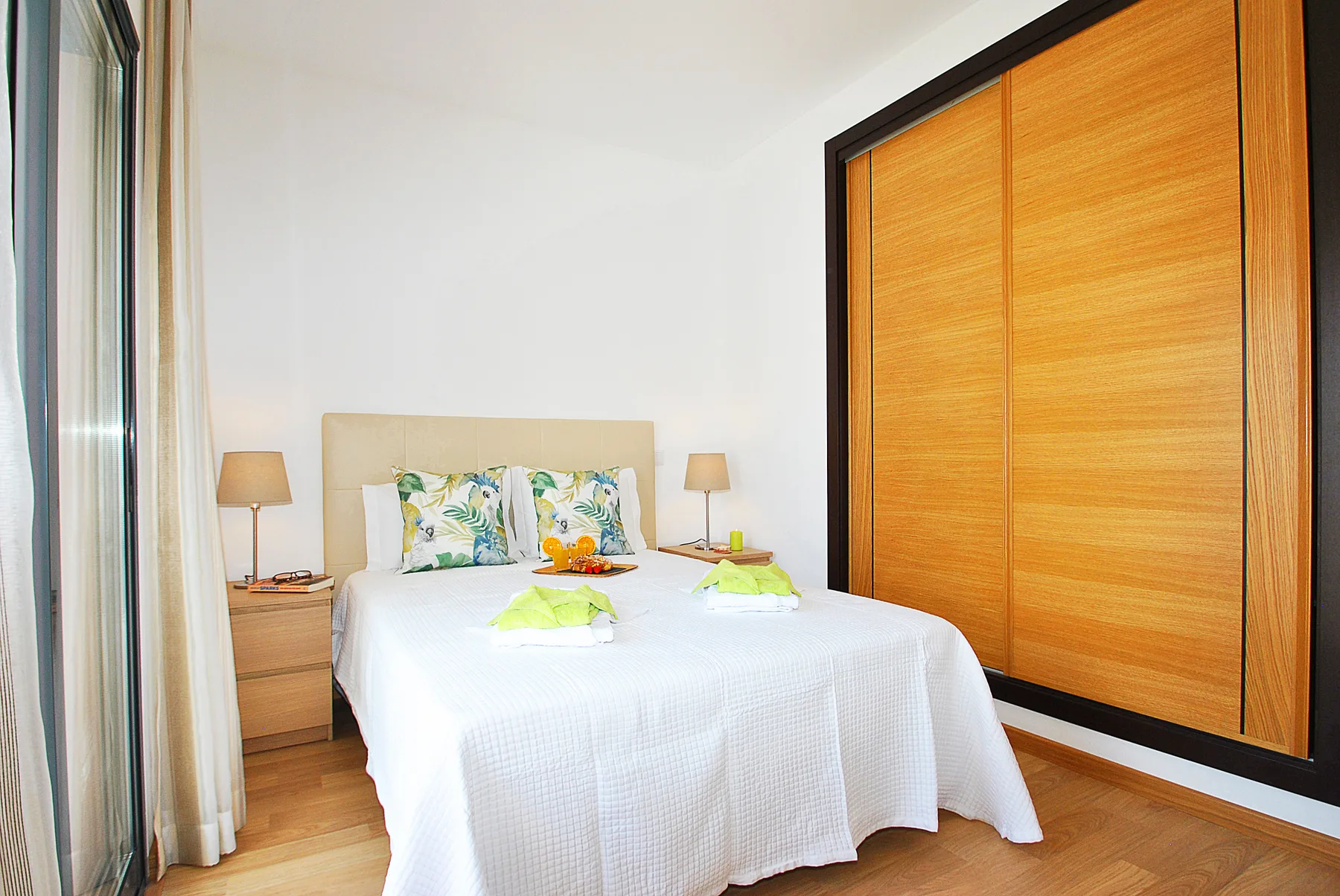 Un dormitorio luminoso con una cama blanca y un gran armario de madera.