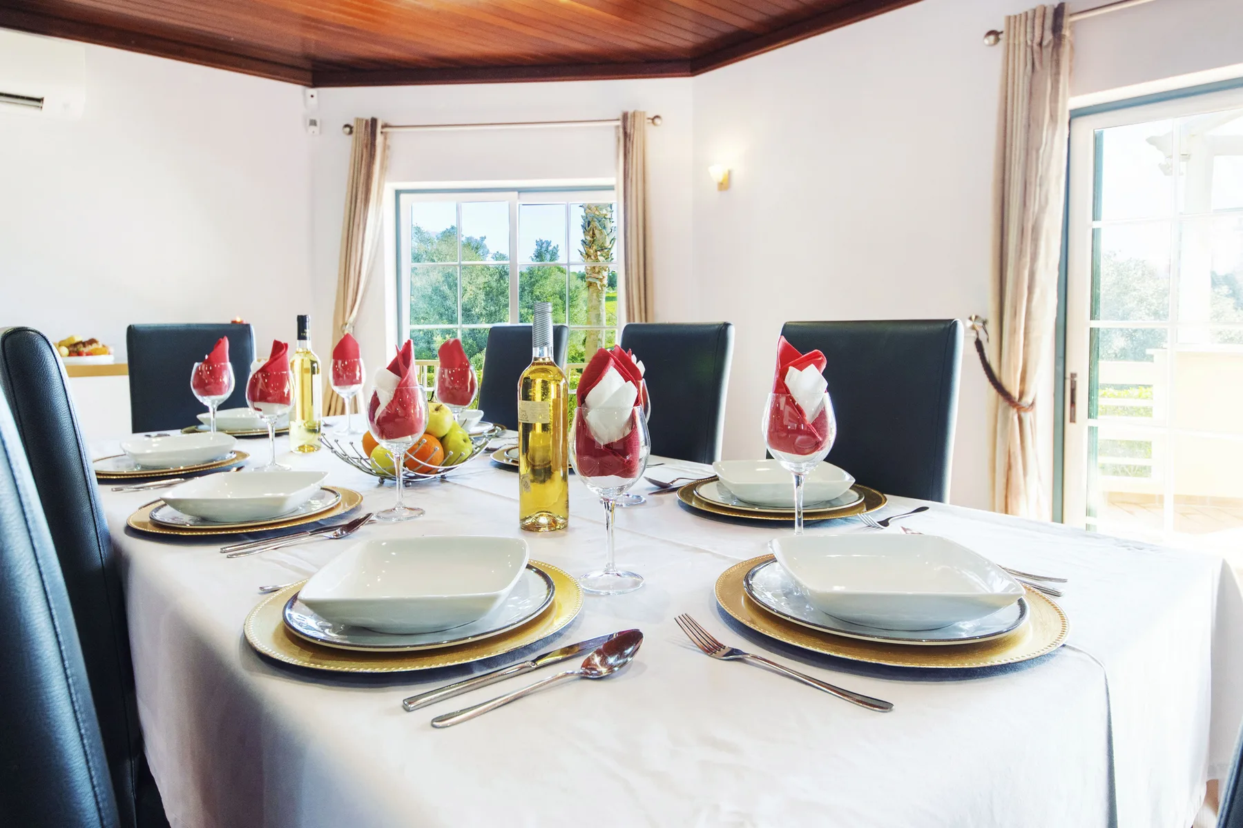 A dining room with a table set for a meal beside large windows.