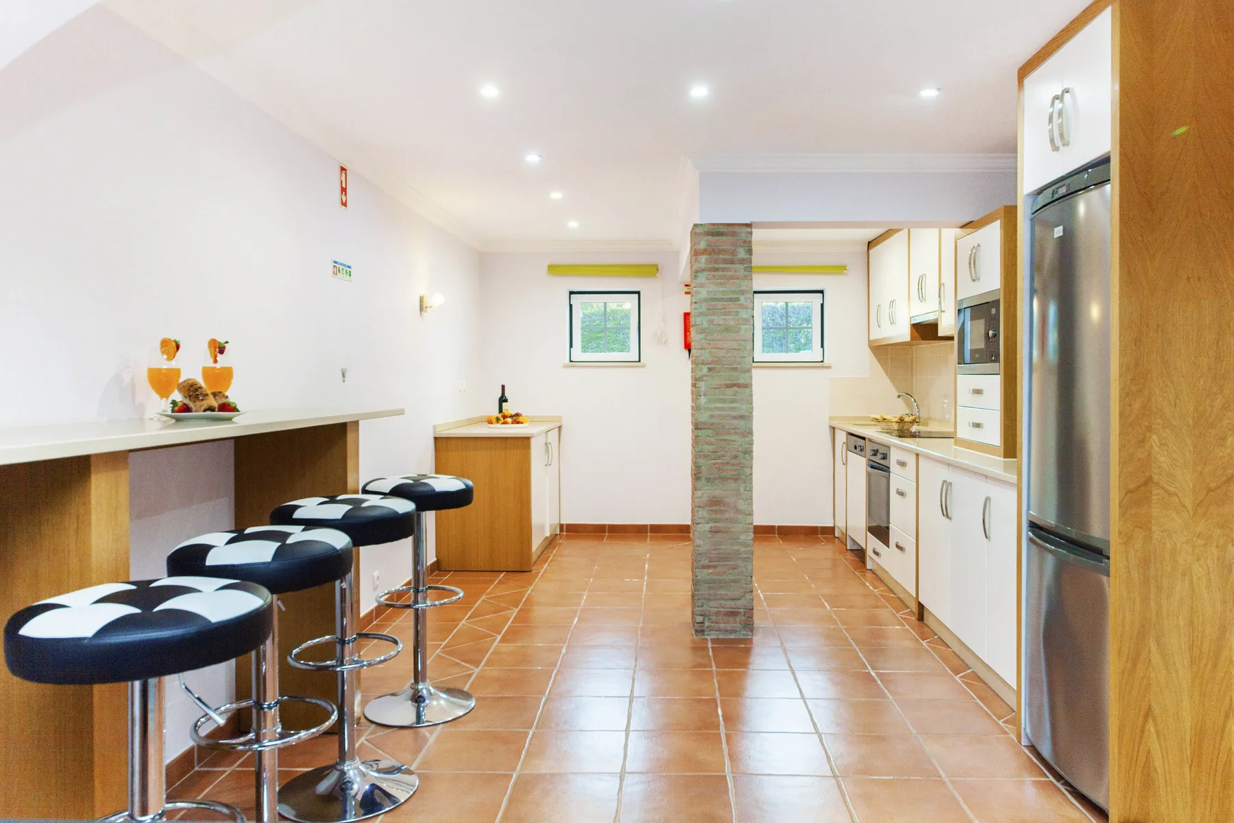 A bright kitchen with a long counter, bar seating, and tiled flooring.