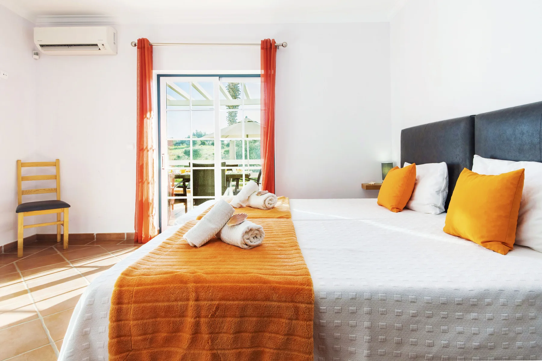A bright bedroom with a large bed dressed in white and orange linens.