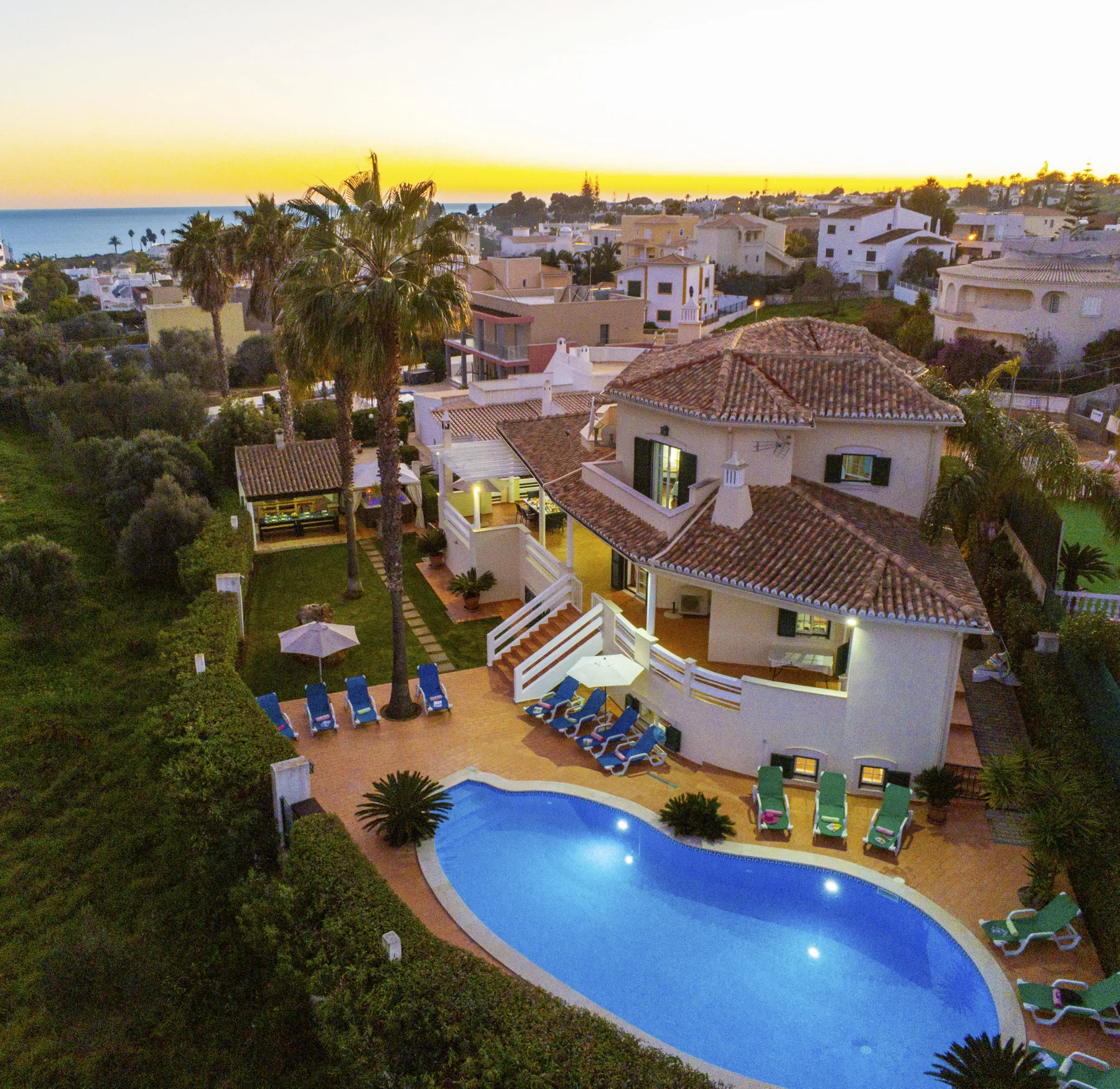 Aerial view of a house, swimming pool, and surrounding homes at sunset.