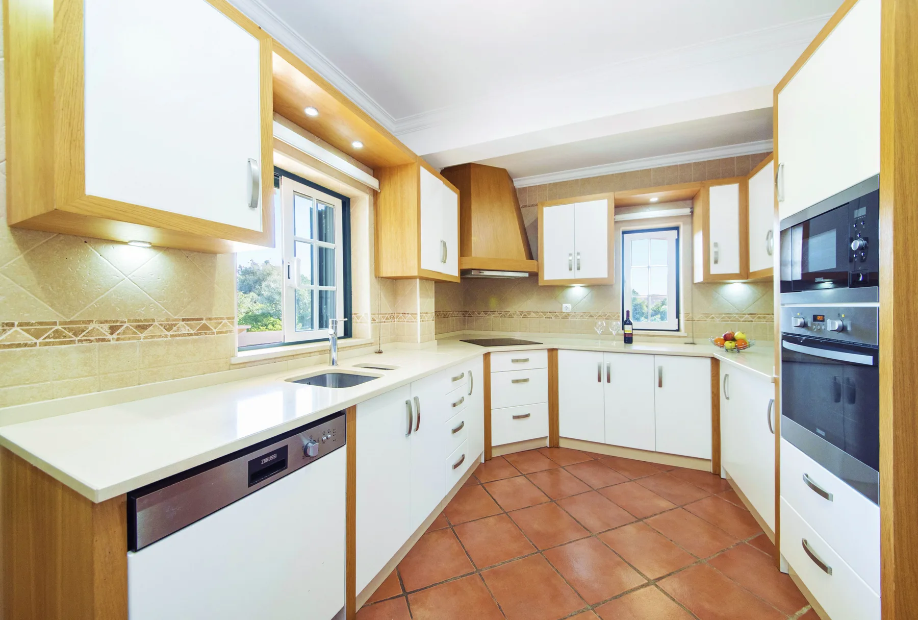 A bright kitchen with white cabinets, wood trim, and tiled flooring.