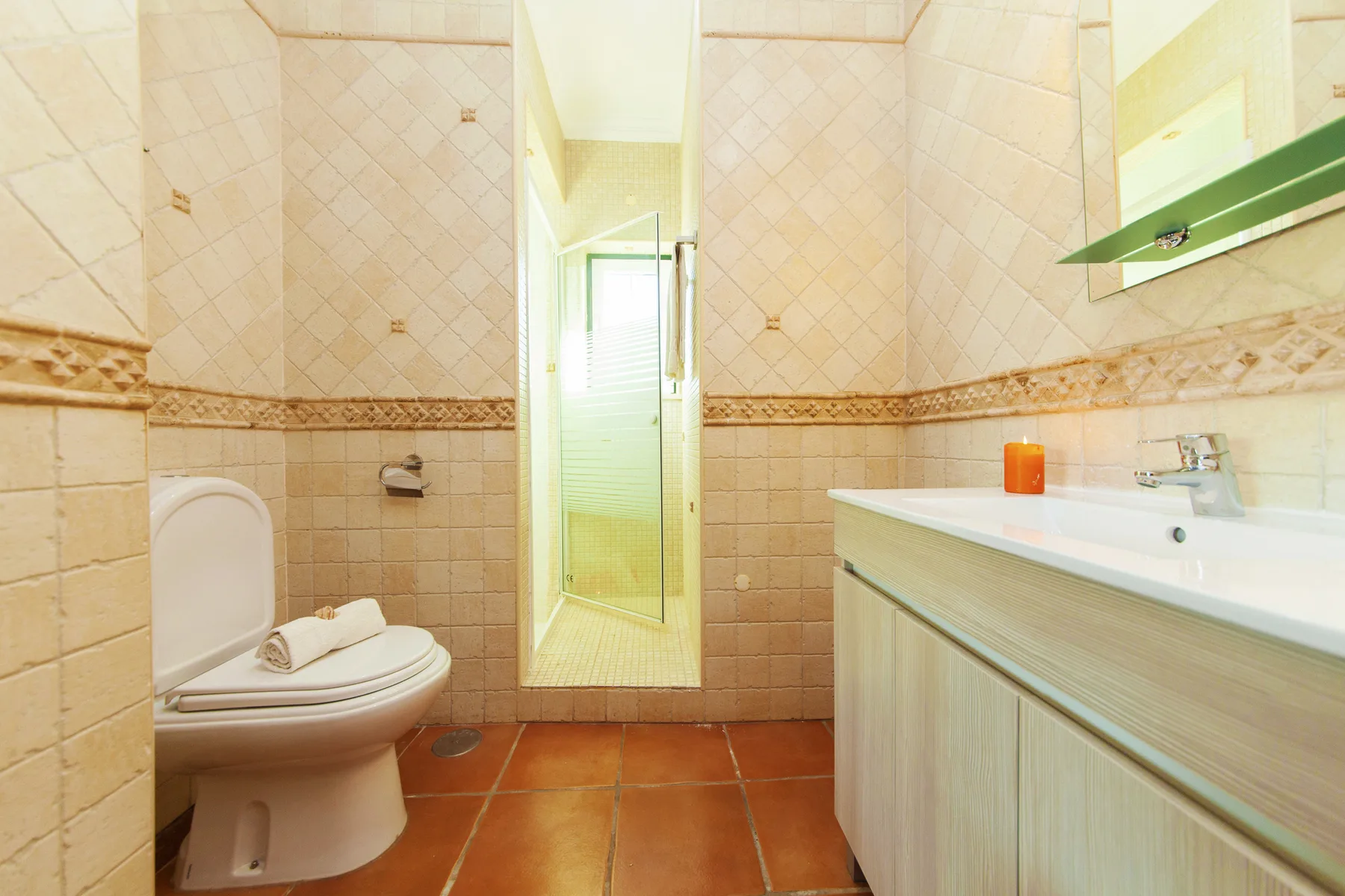 A tiled bathroom with a toilet, sink, and glass shower enclosure.