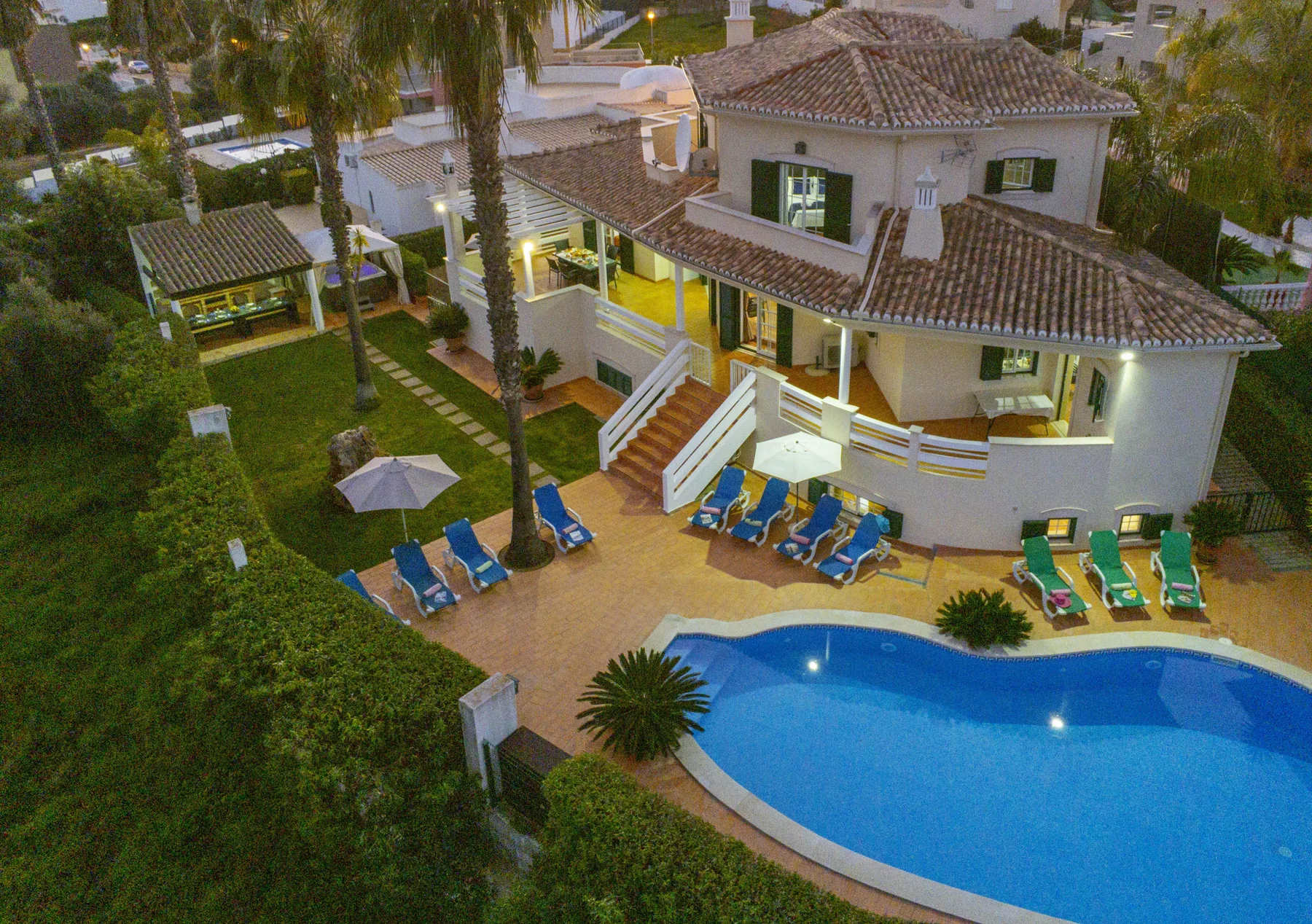 A large house overlooks a curved swimming pool and a patio with lounge seating.