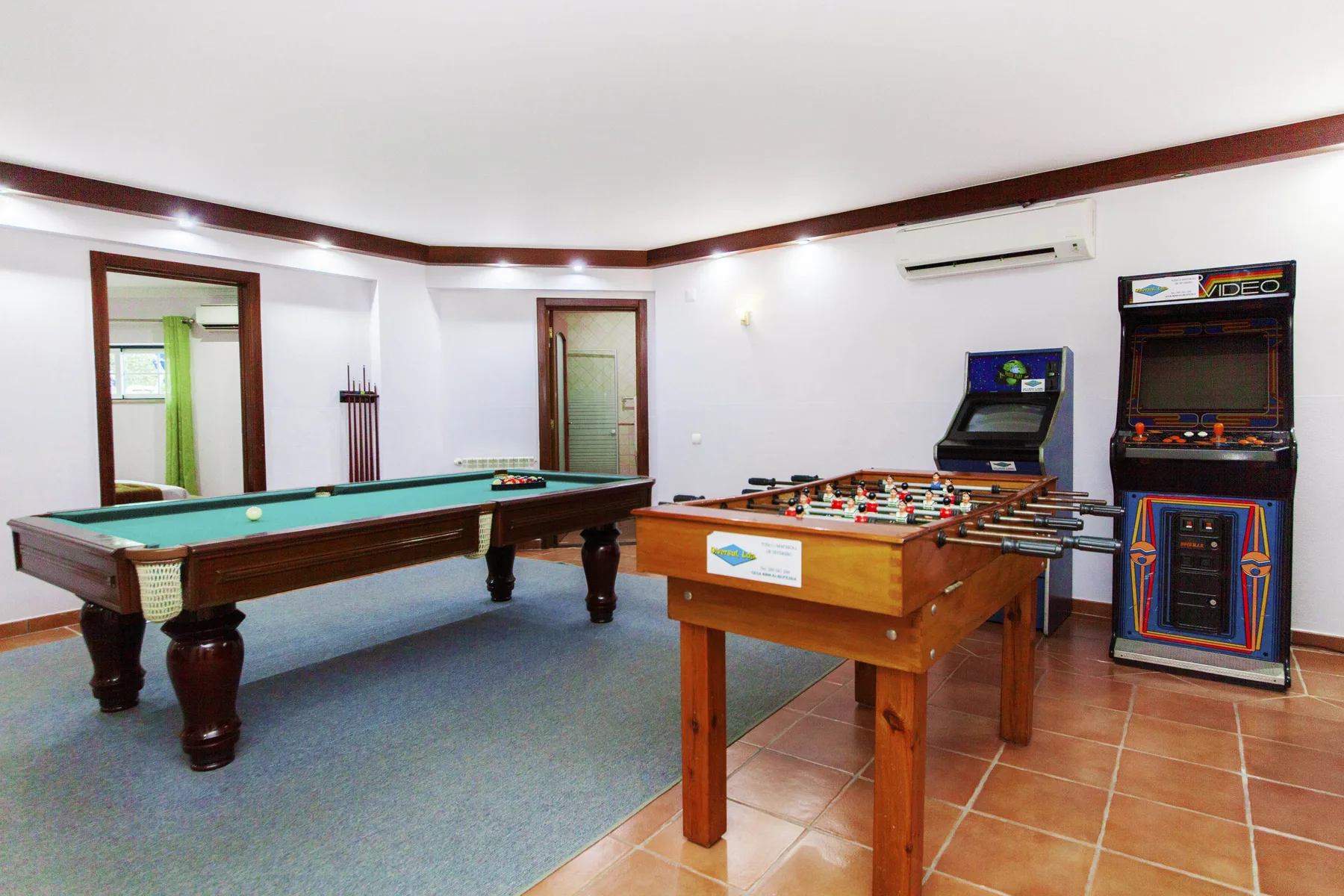 A game room with a pool table, foosball table, and arcade machines.