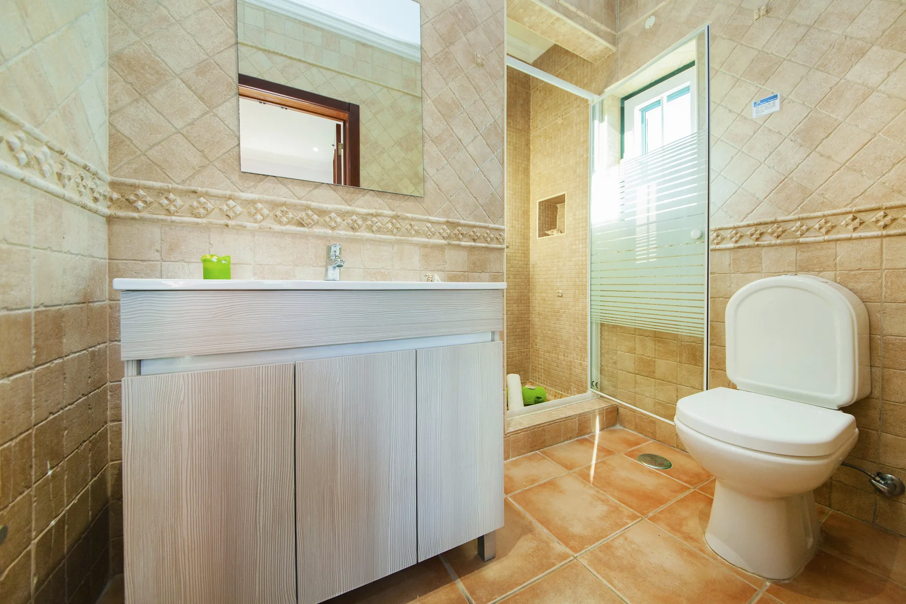 A tiled bathroom with a sink vanity, mirror, glass shower, and toilet.