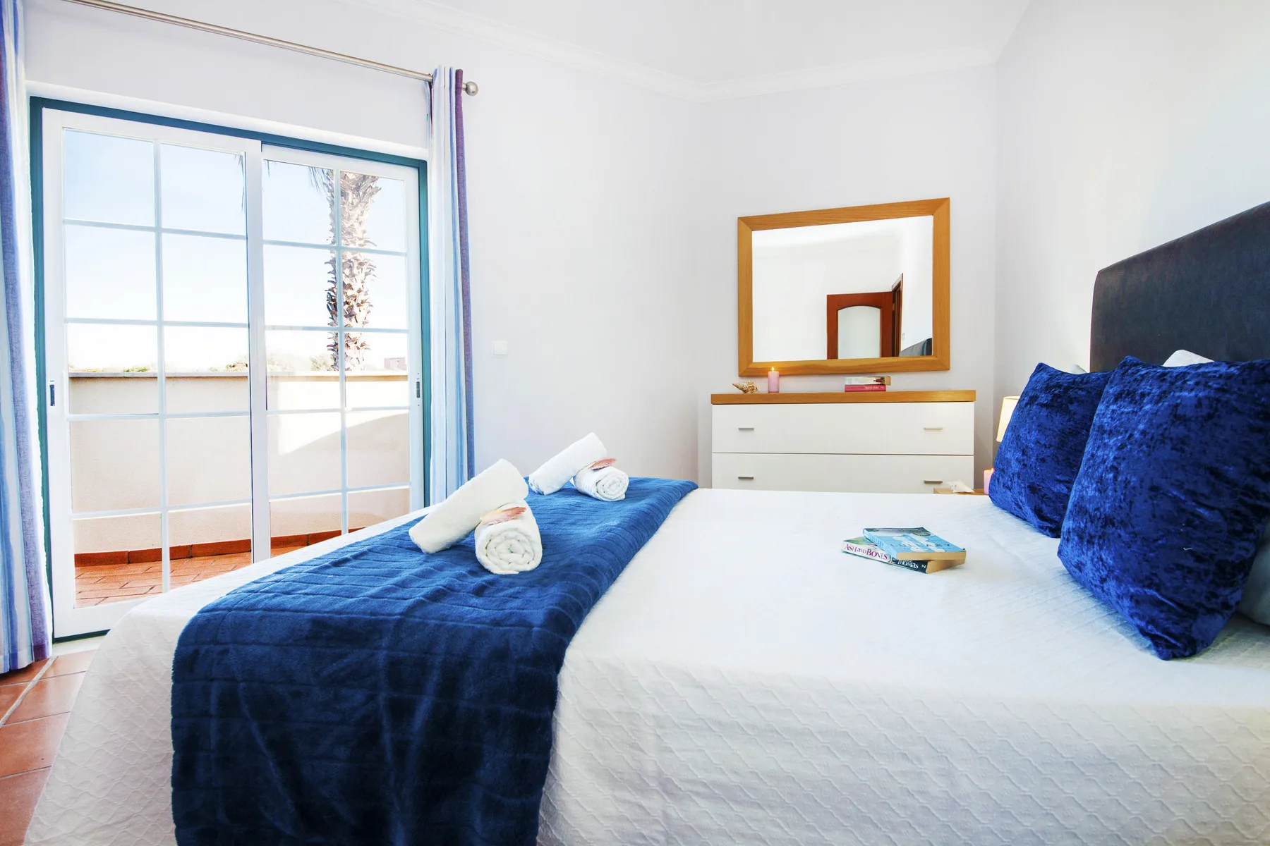 A bright bedroom with a bed dressed in white linens and deep blue accents.