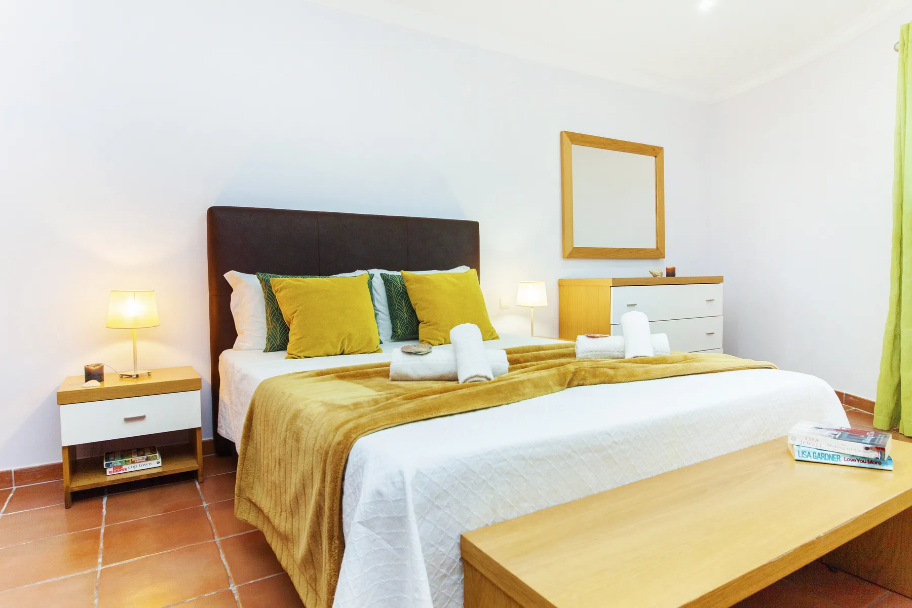 A bedroom with a bed dressed in white and gold bedding and bright accent pillows.