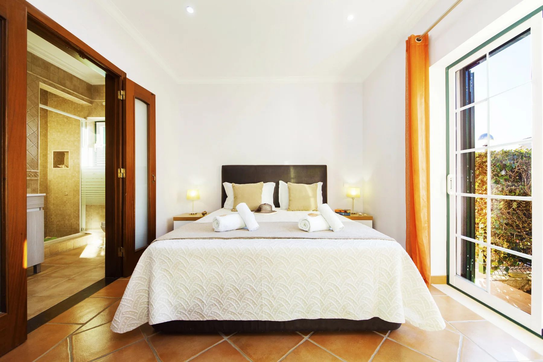 A bright bedroom features a neatly made bed beside a glass door.