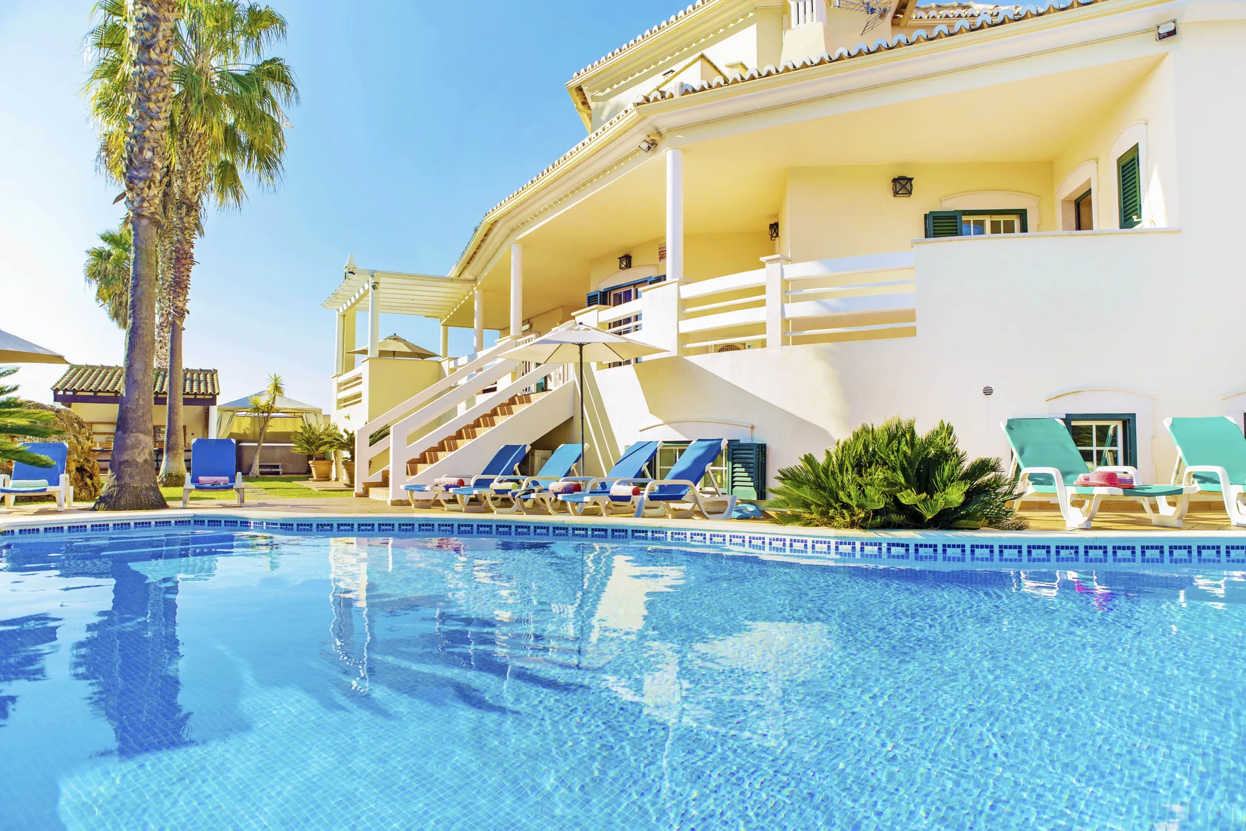 A swimming pool sits beside a white building with outdoor seating.