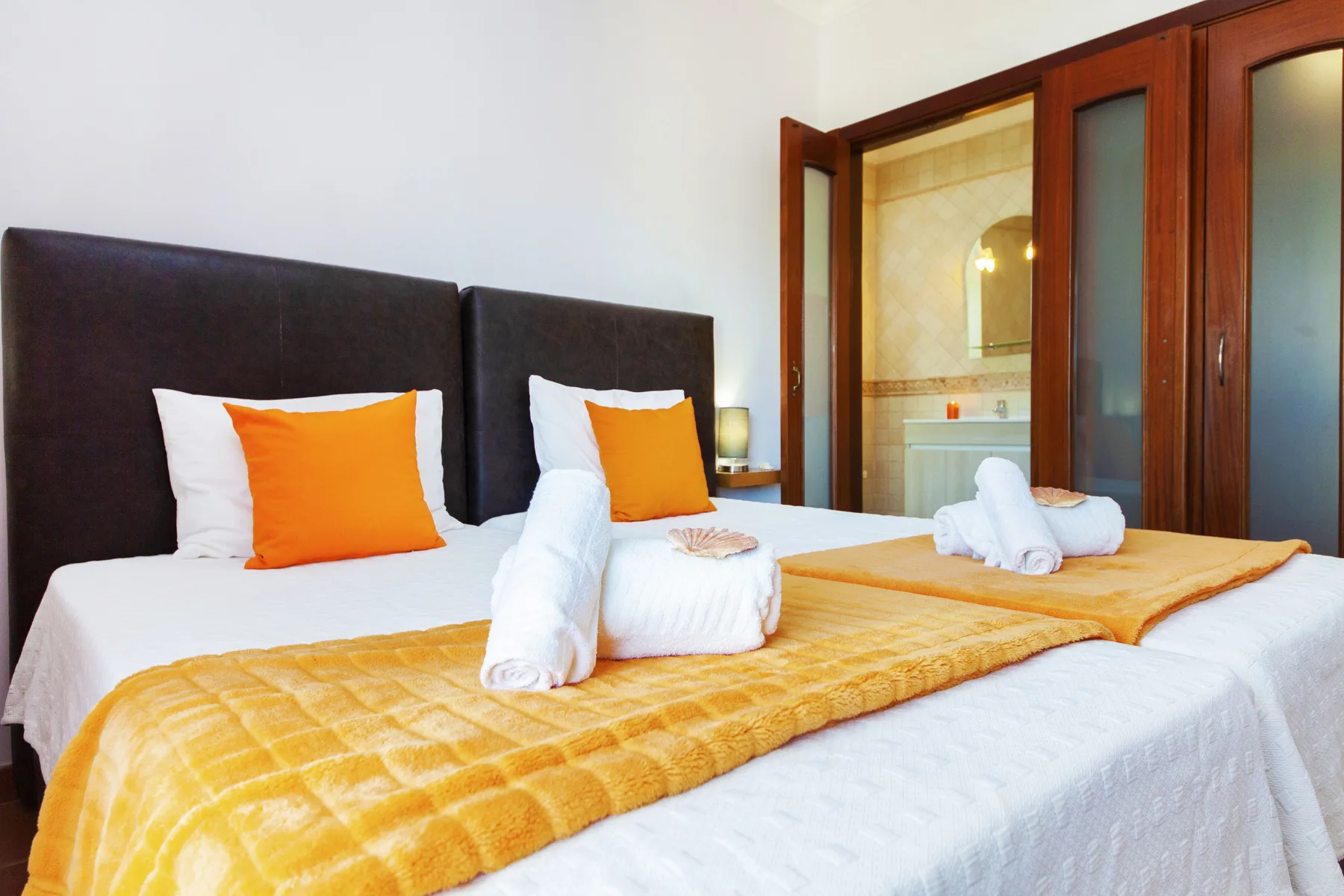 A bedroom with neatly made beds and bright orange pillows.
