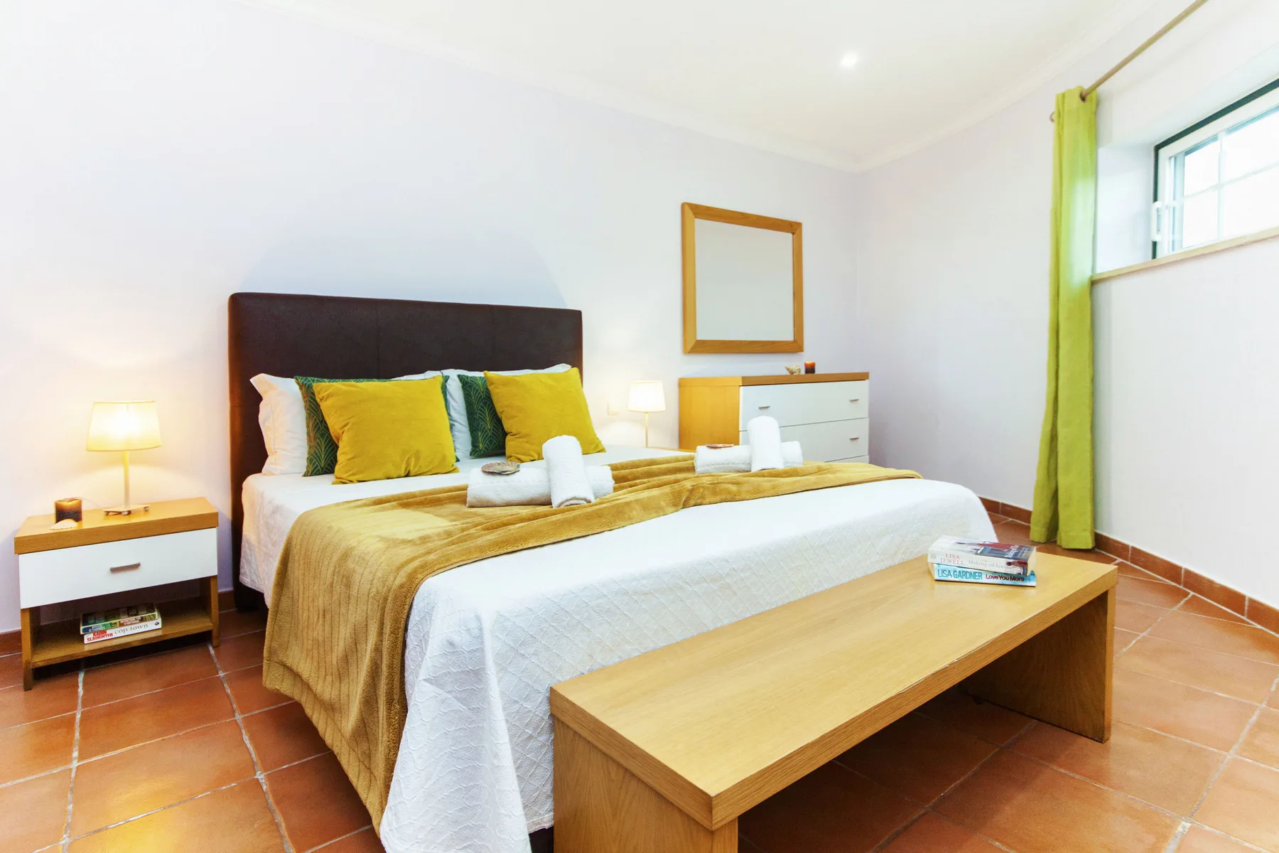 A bright bedroom with a neatly made bed and a wooden bench at its foot.