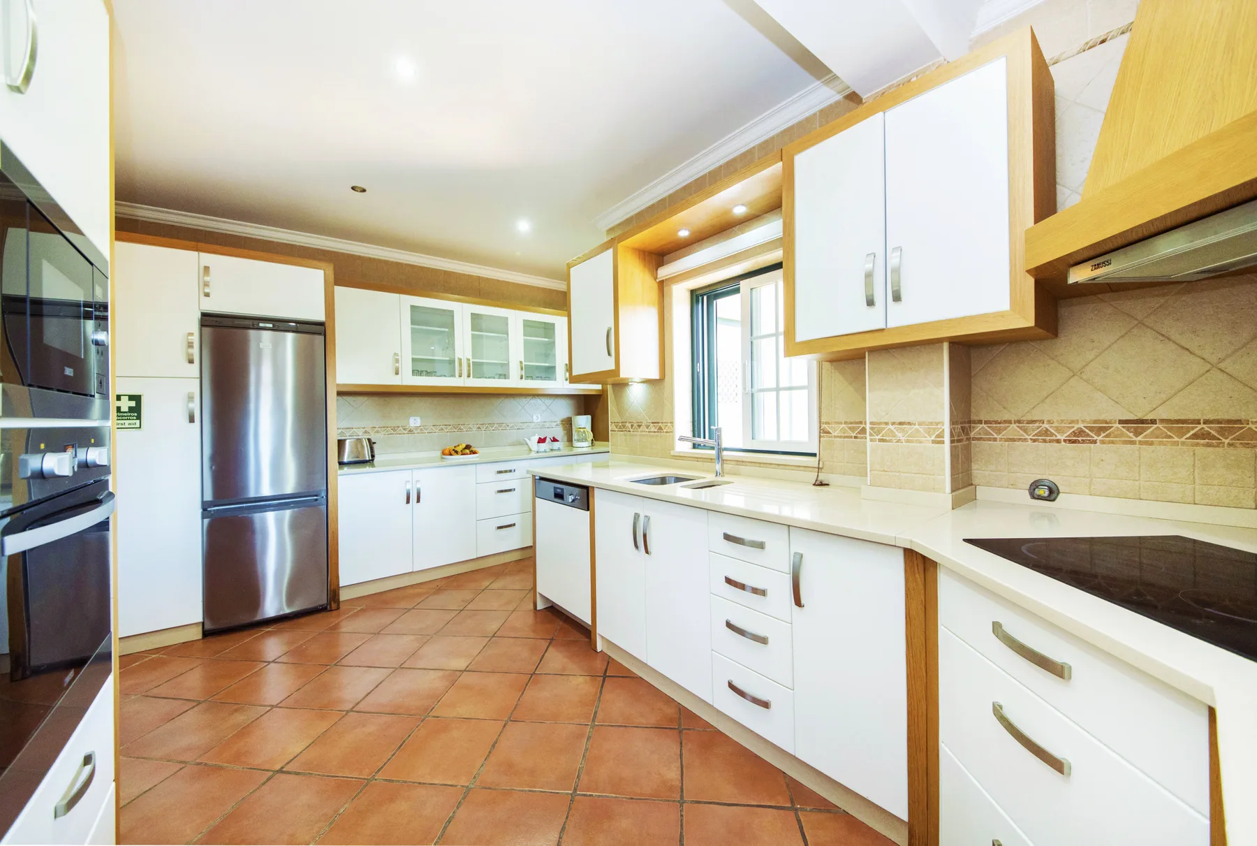 A bright kitchen with white cabinets, tiled counters, and a window.