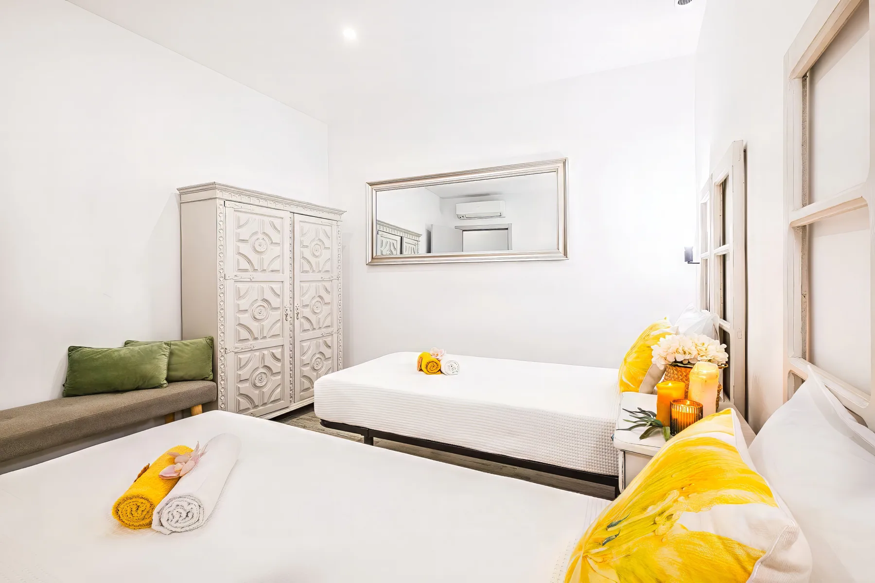 A bright bedroom with two beds, a carved wardrobe, and yellow accents.
