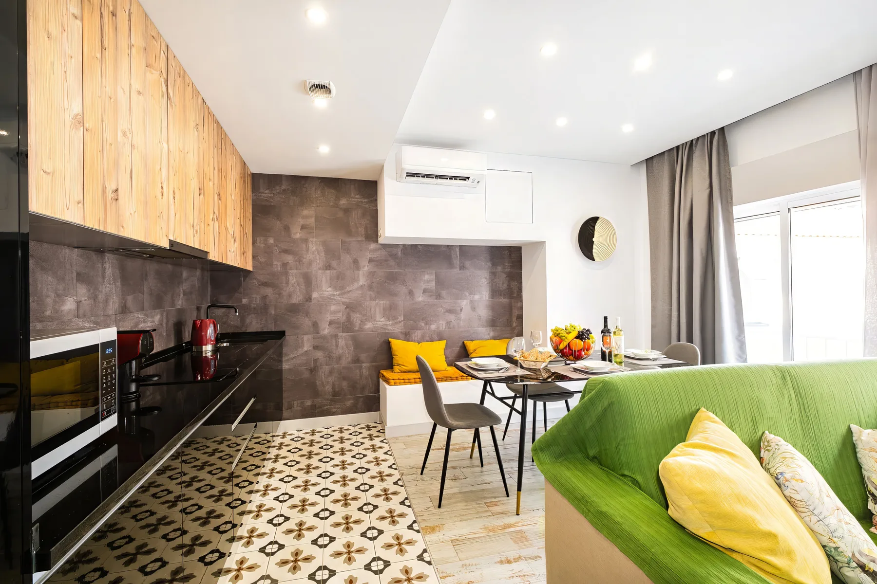 A bright open-plan kitchen and living area with a dining table and green seating.
