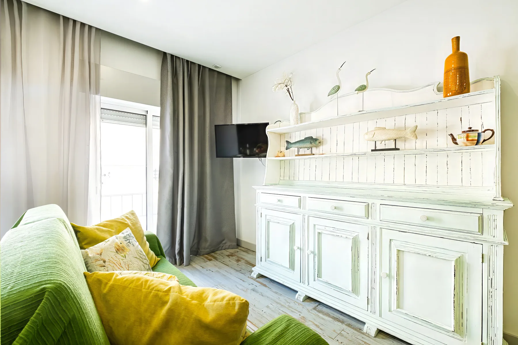 A bright living room with green seating beside a white display cabinet.