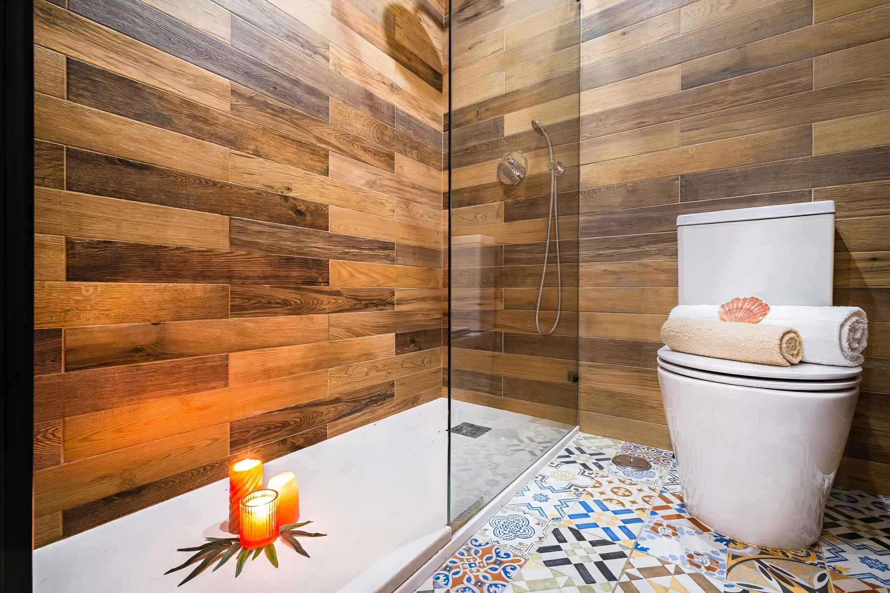 A bathroom with a glass shower, toilet, and wood-look wall tiles.
