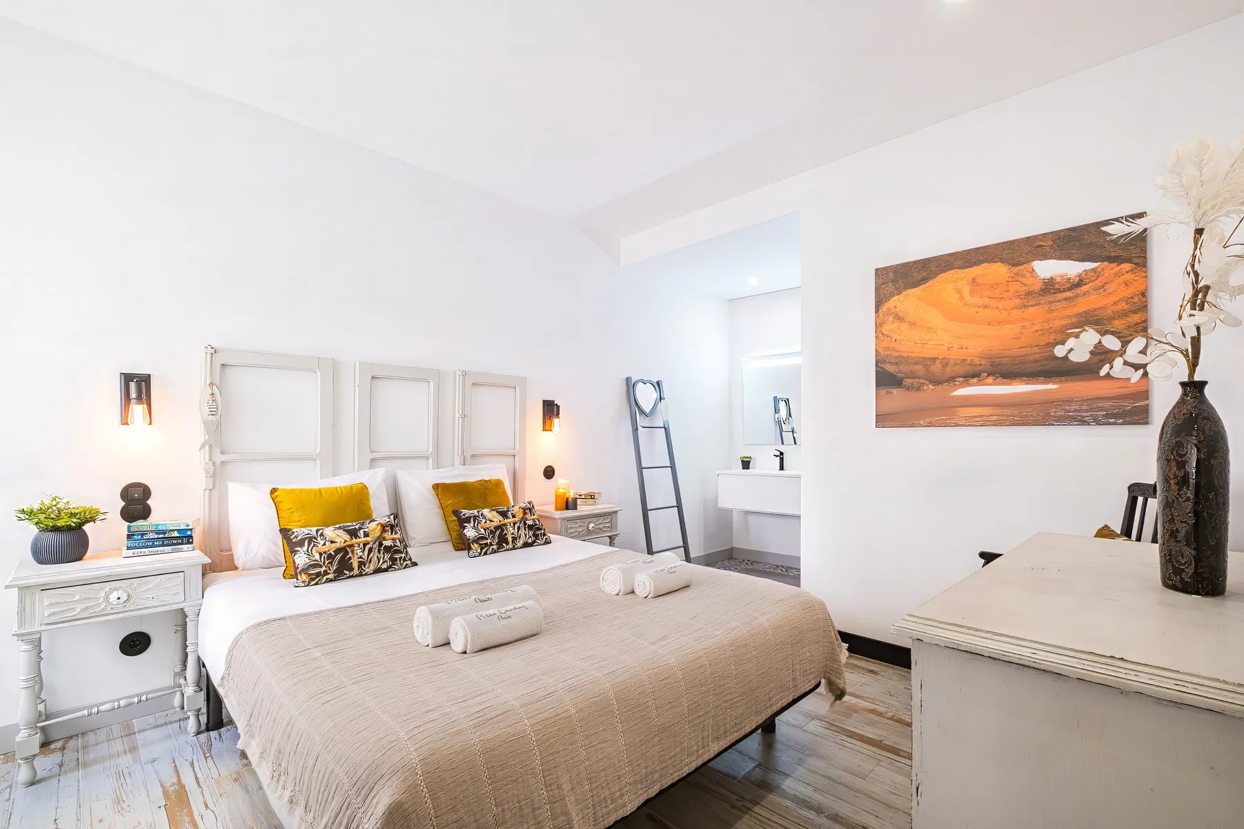 A bright bedroom with a large bed and an orange-toned landscape painting.
